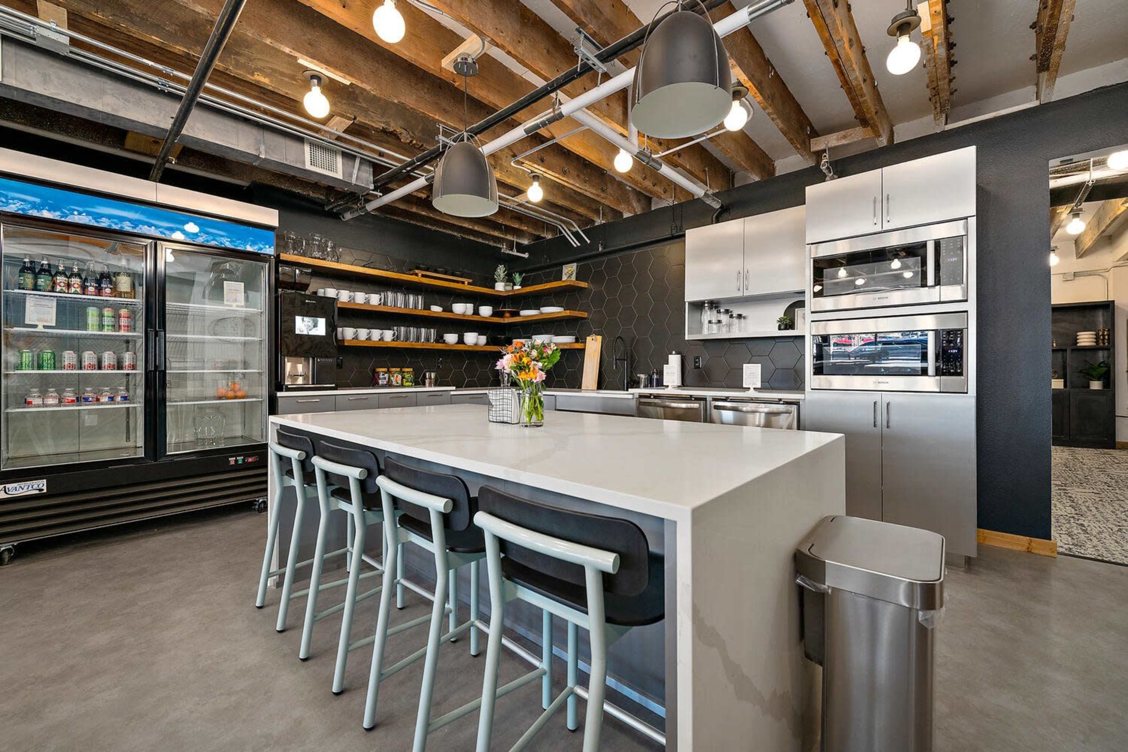 A modern kitchen with a large white island, seating on one side, stainless steel appliances, and a beverage cooler against the wall.
