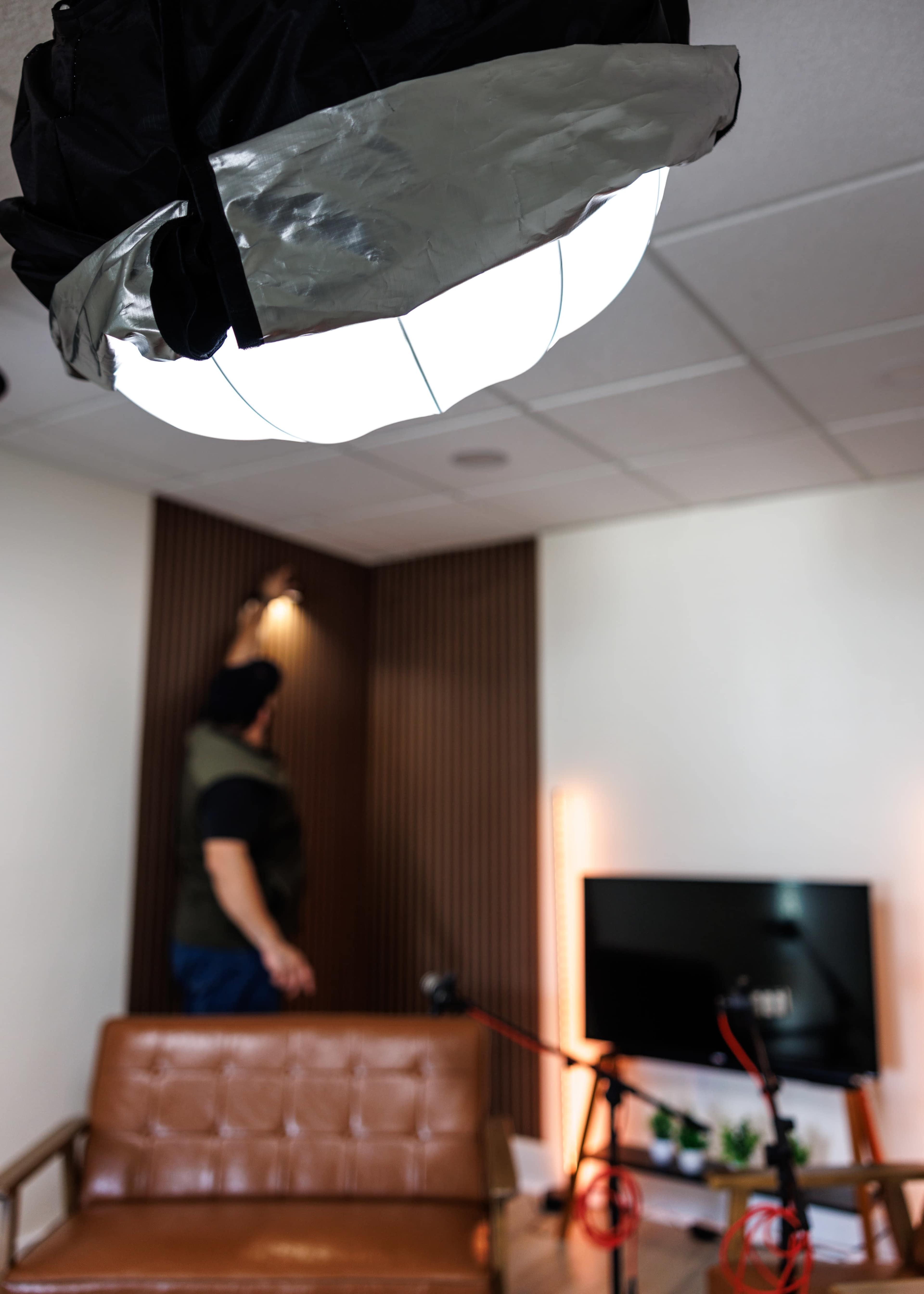A person adjusts a lighting fixture in a neatly arranged room with a brown sofa and a television setup.