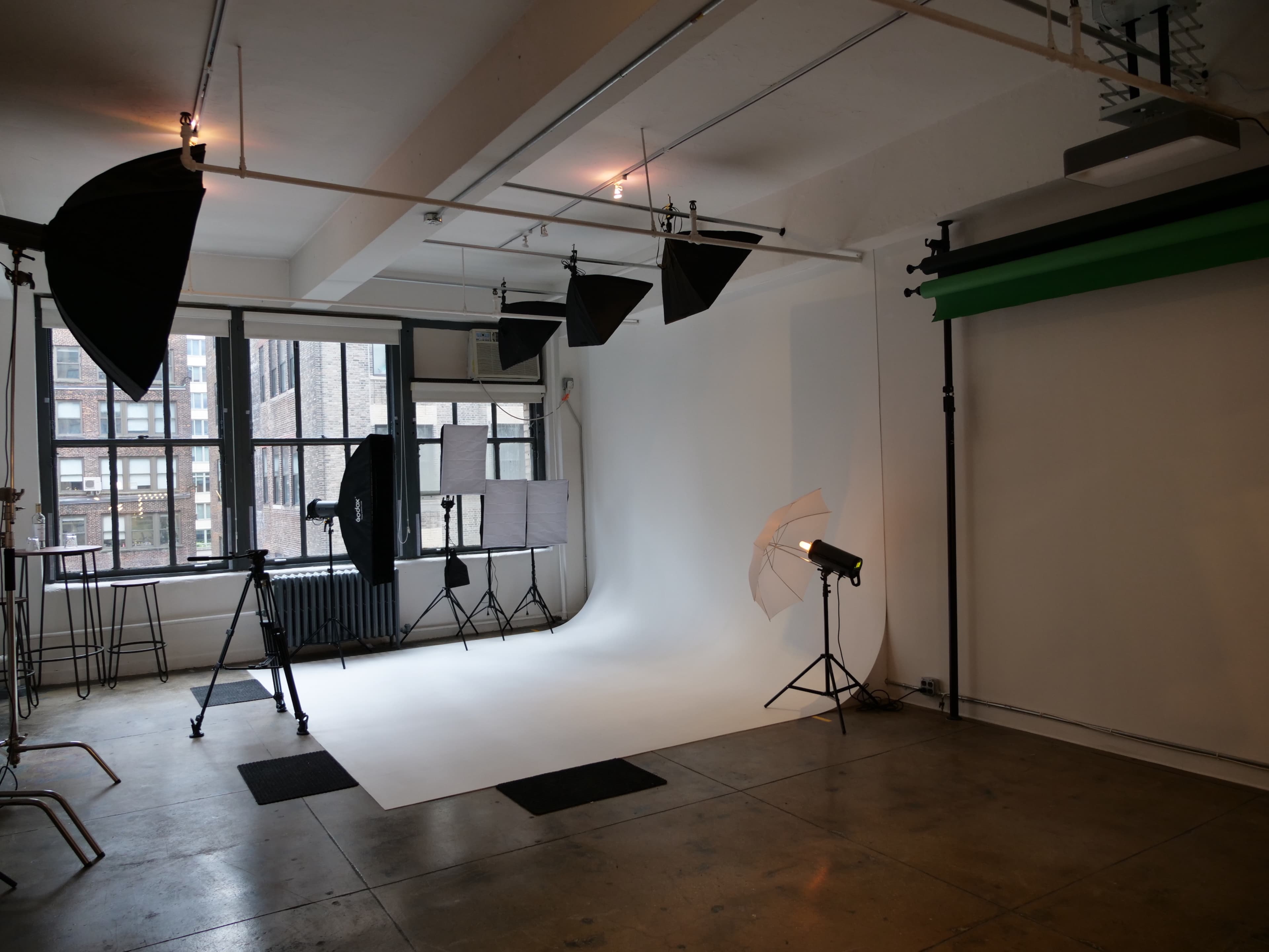 A photography studio with a white backdrop, various lighting equipment, and a concrete floor.