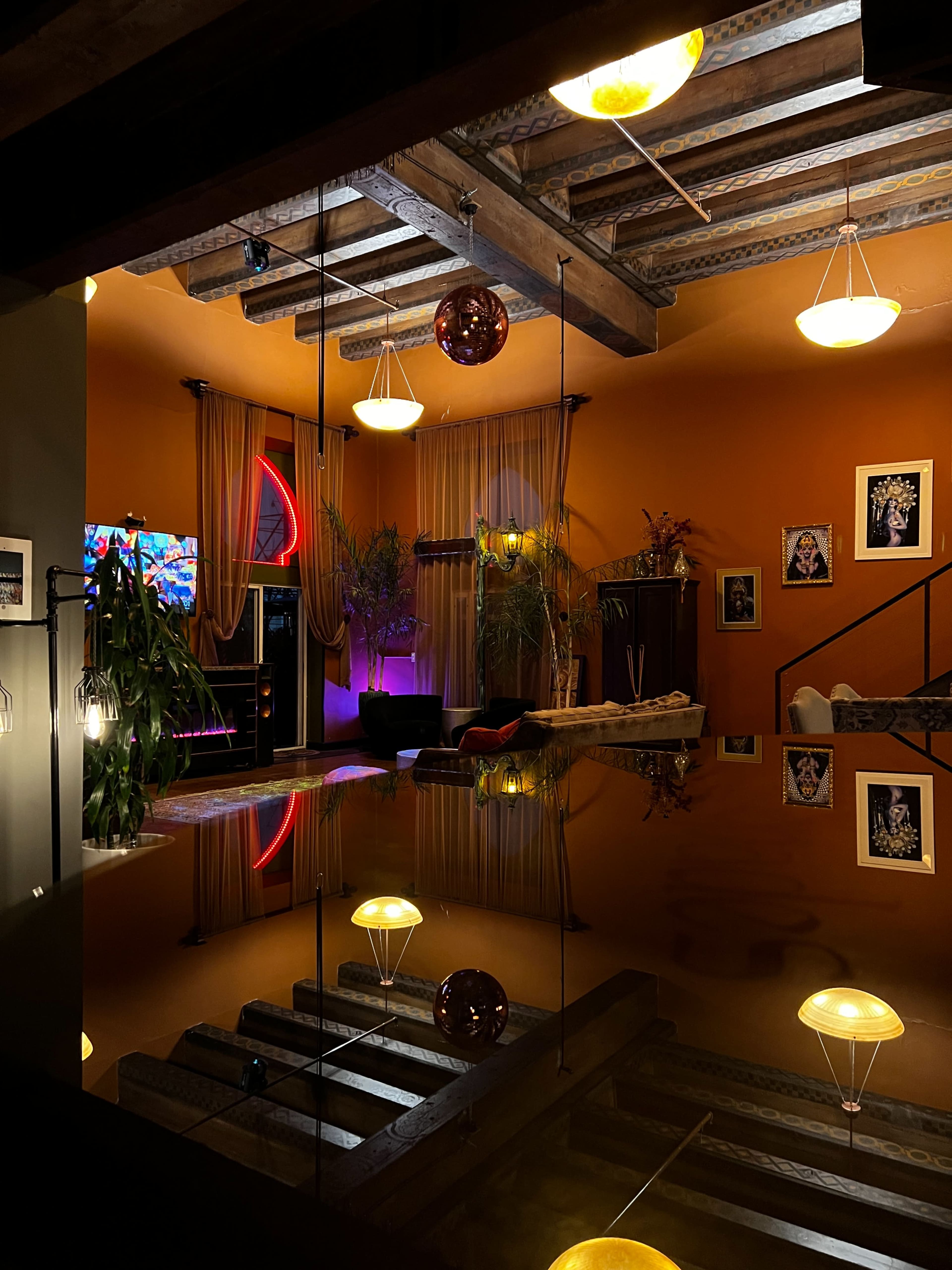 A stylishly decorated interior space with wooden beams, colorful lighting, plants, and a reflective surface.