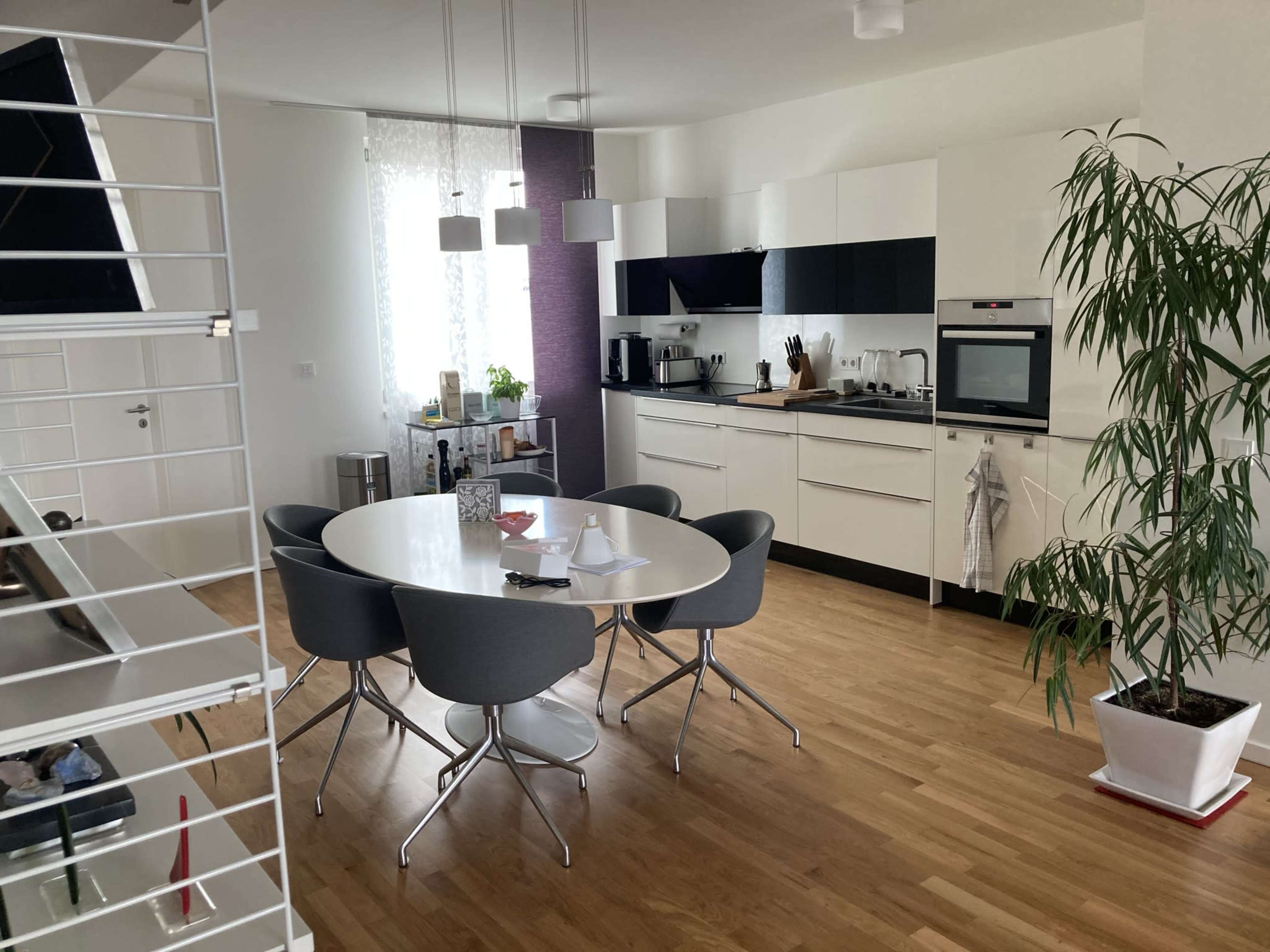 A modern kitchen and dining area features a round table surrounded by gray chairs, with a minimalist design and hardwood flooring.