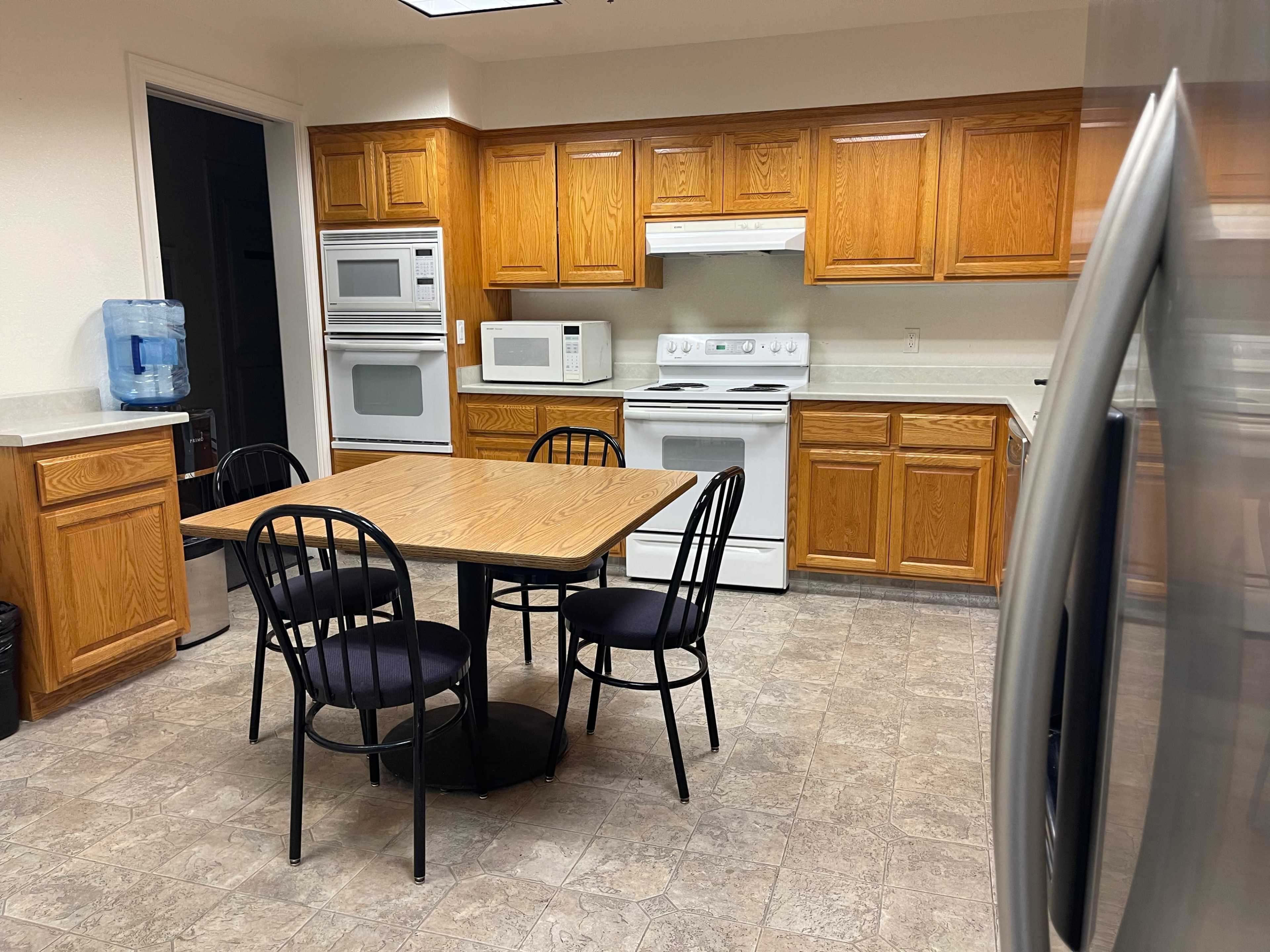 A kitchen with wooden cabinets, a table and four chairs, and various appliances including a microwave and a refrigerator.