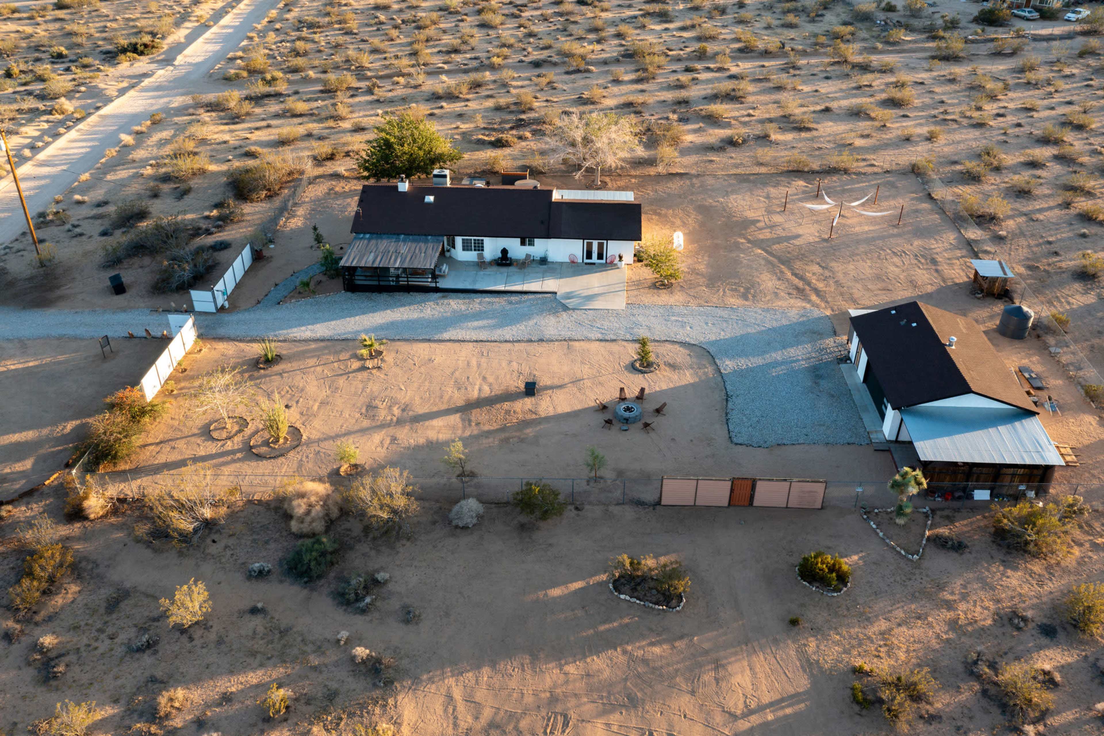 The image shows an aerial view of a landscaped desert property with two buildings, a gravel path, and sparse vegetation surrounding them.