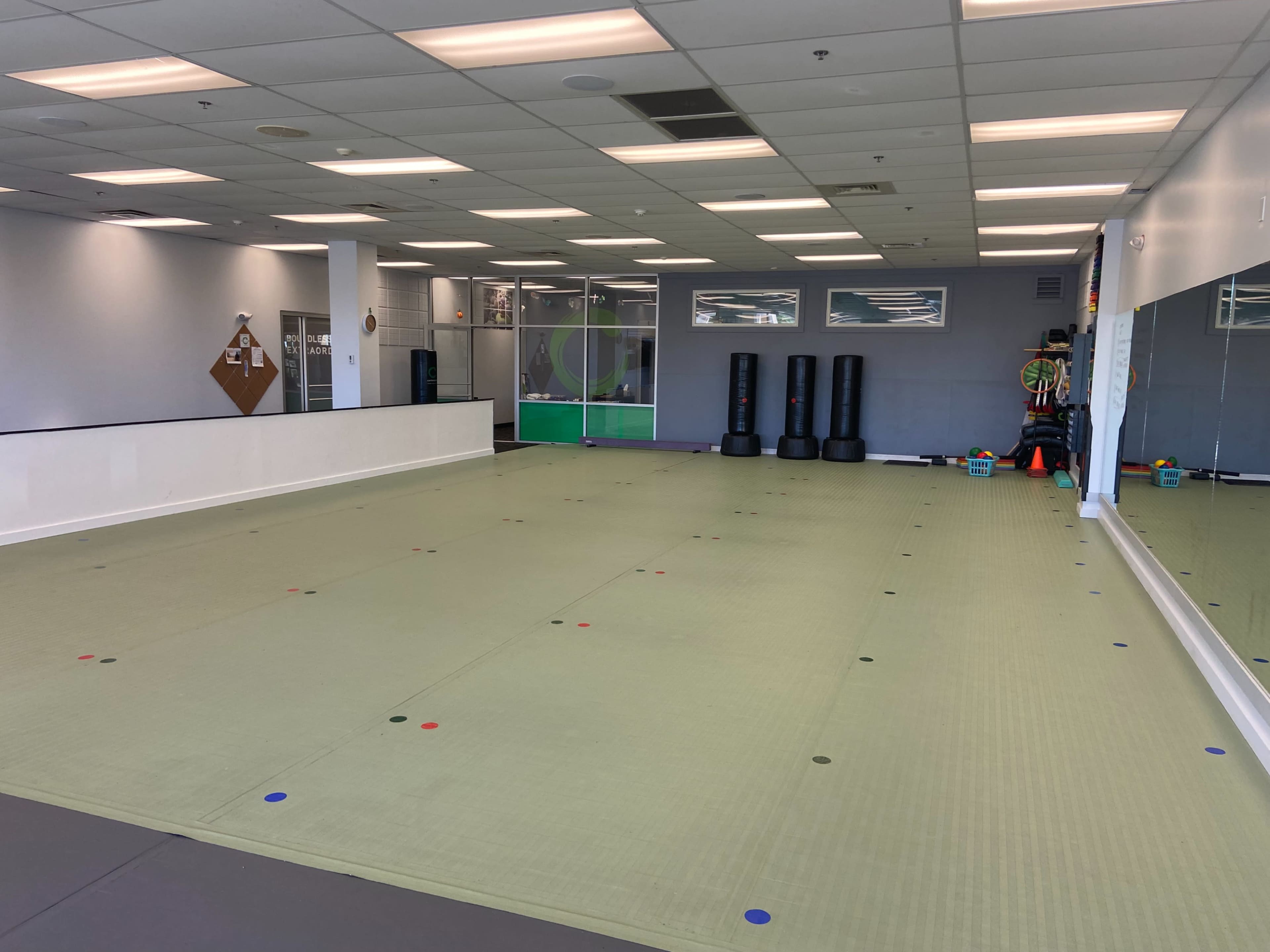 An empty martial arts studio with a padded floor, large mirrors on one wall, and equipment stored in a corner.