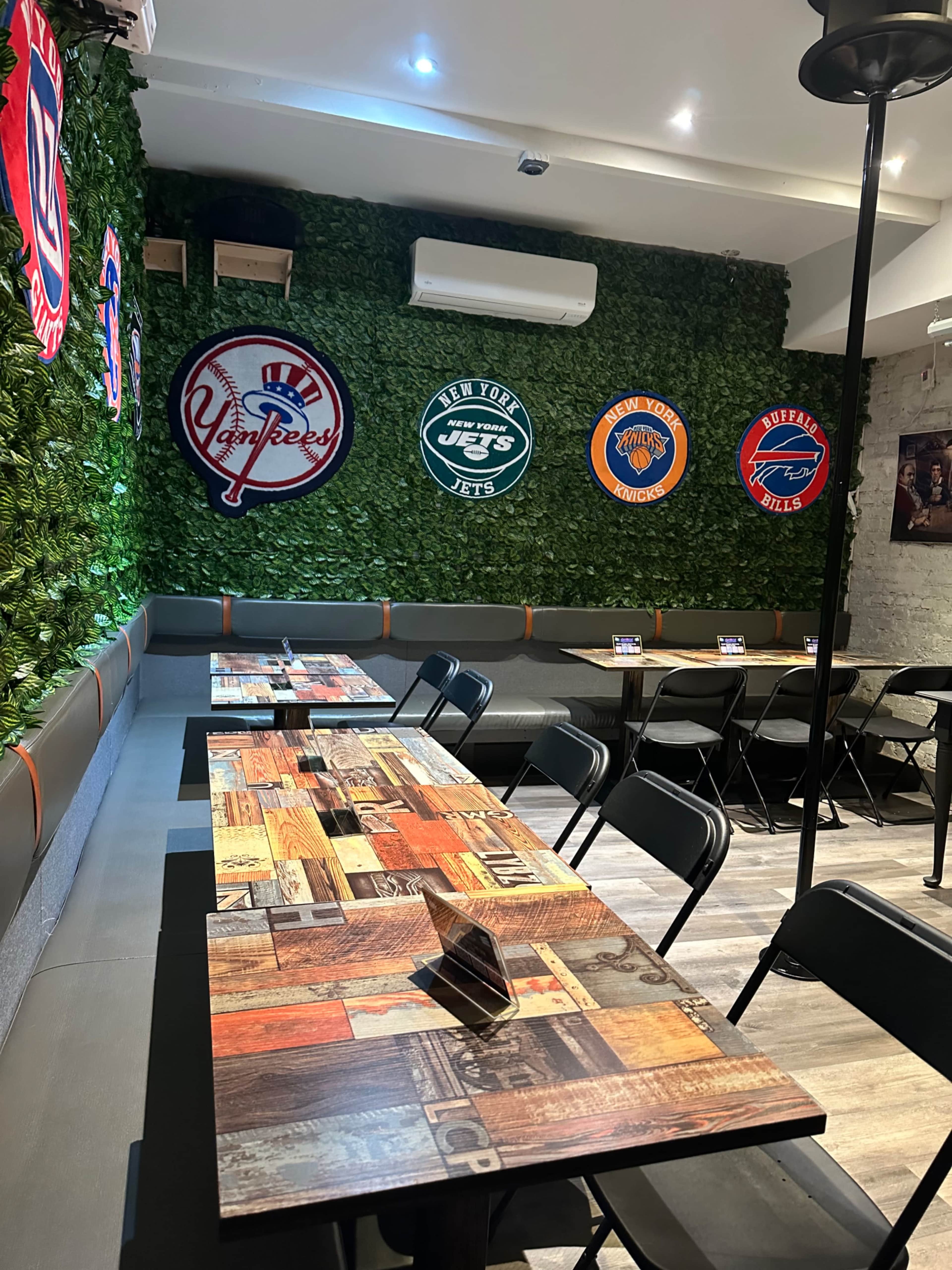 The image shows a cozy restaurant with wooden tables, green wall decoration, and sports memorabilia featured on the walls.