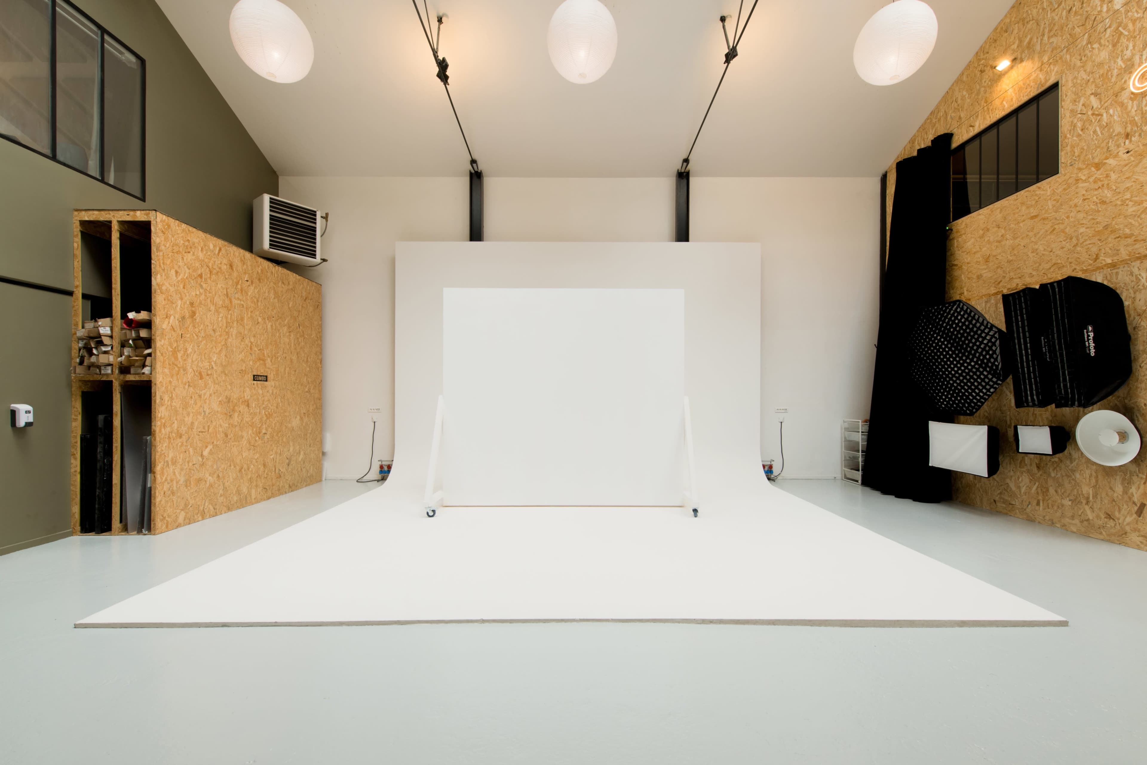 A minimalist photo studio with a white backdrop and various photography equipment arranged around the space.