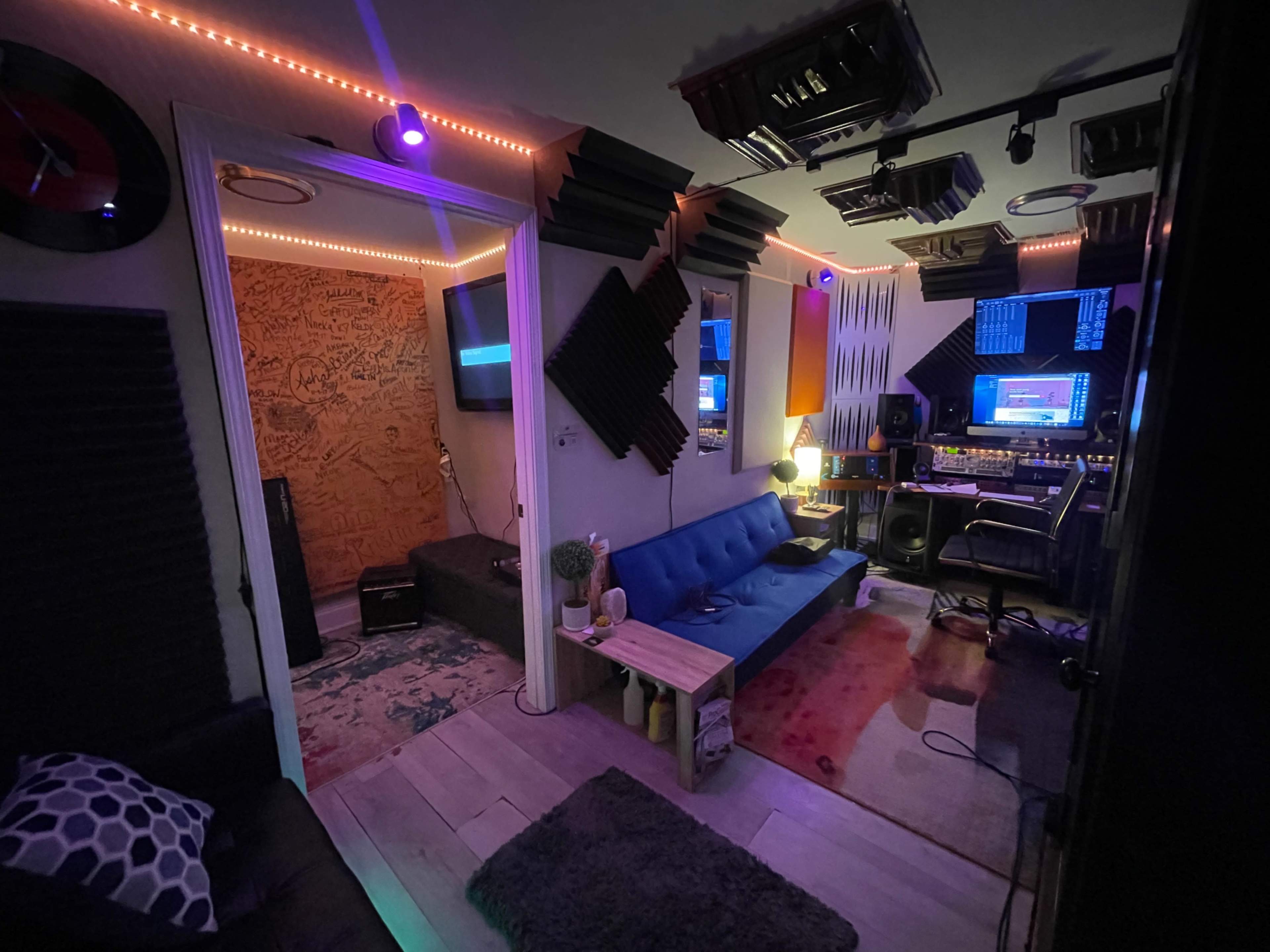 A small music studio with soundproofing panels, recording equipment, and a comfortable seating area.