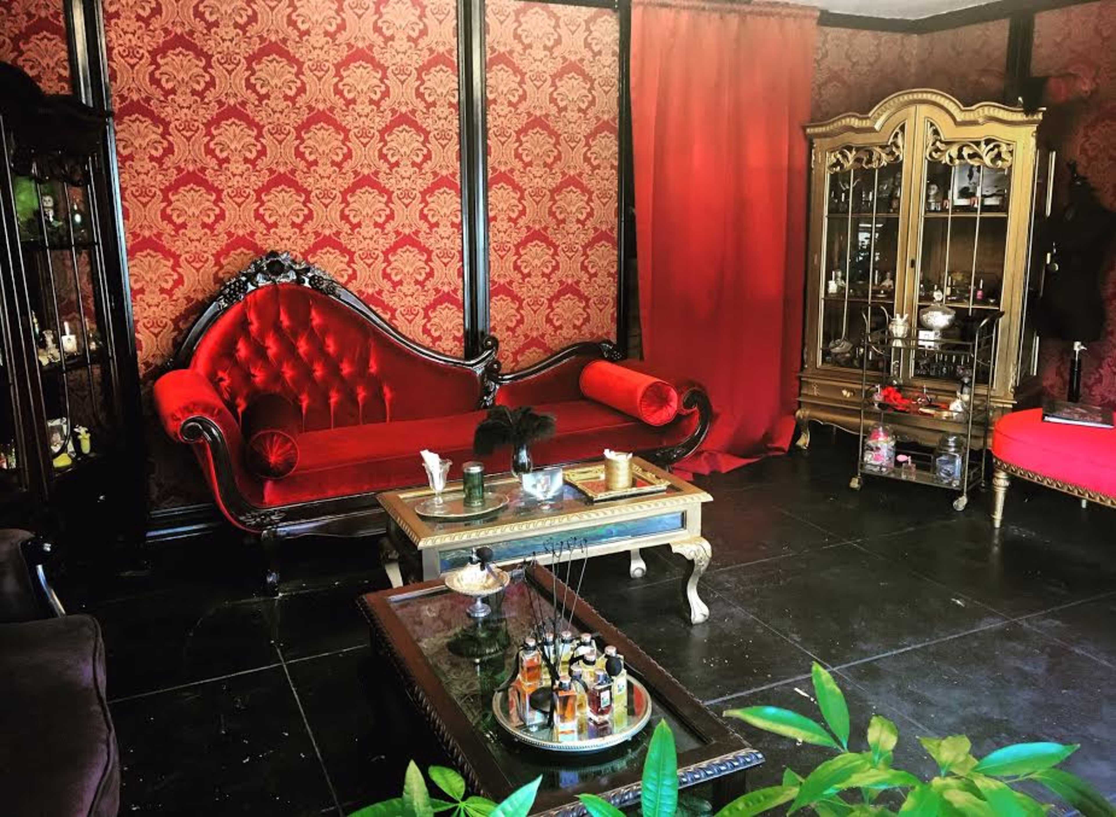 A warmly decorated room featuring a red velvet couch, a glass cabinet filled with decorative items, and a coffee table with various ornaments.