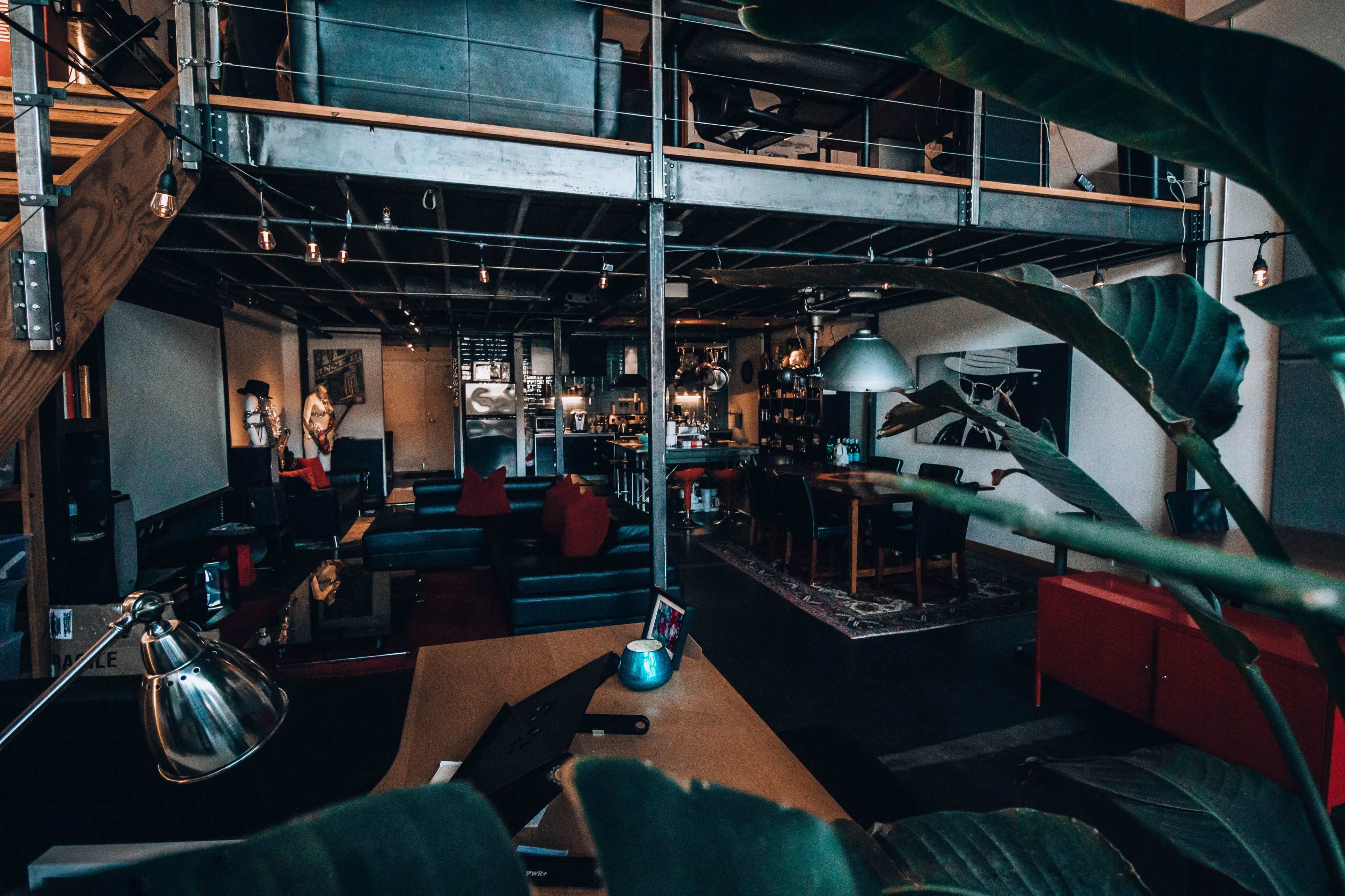A spacious, modern loft with an open layout featuring a living area, dining space, and a kitchen, surrounded by plants and industrial decor.
