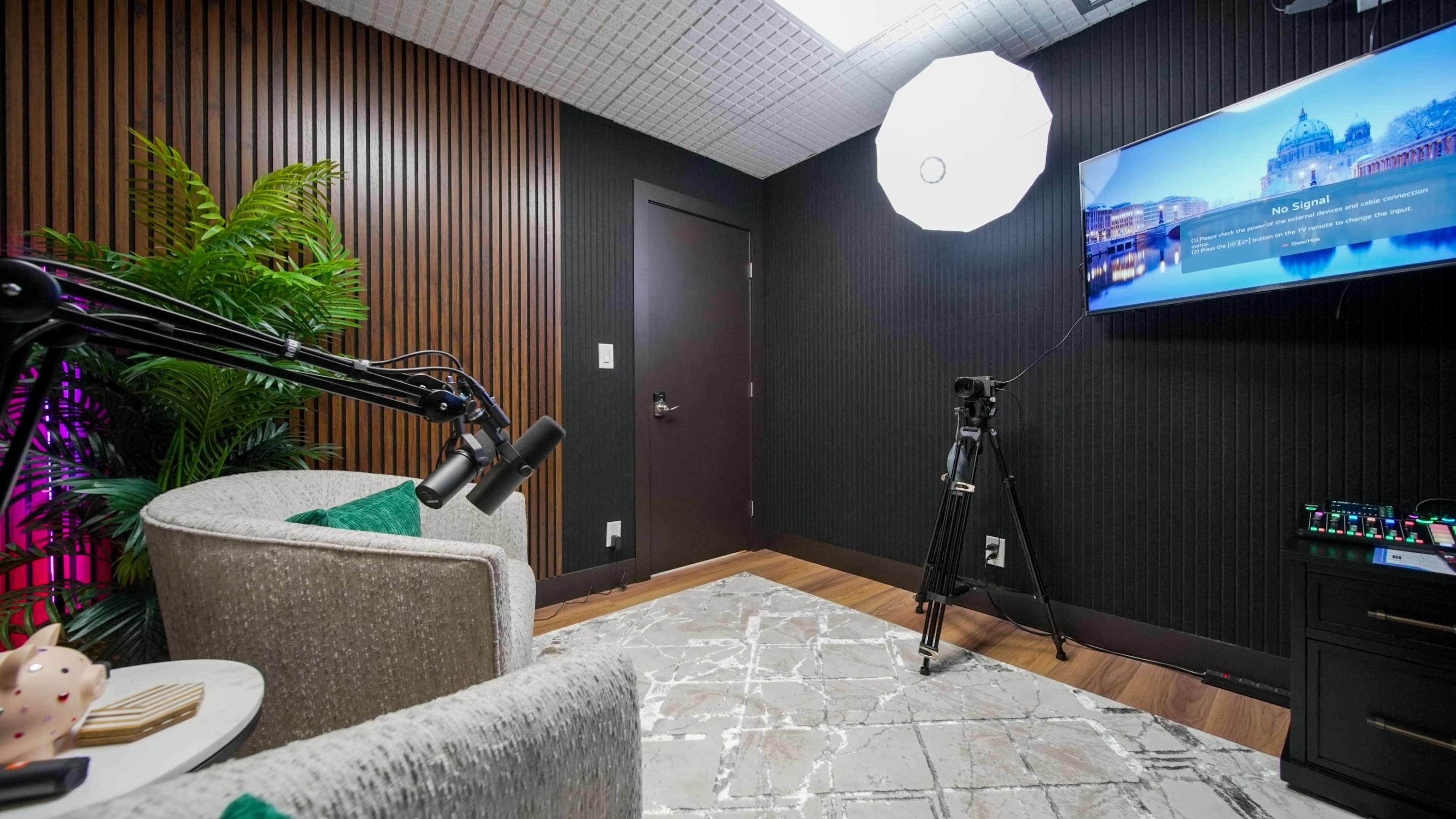 The image shows a well-equipped recording studio with comfortable seating, a lighting setup, and a television screen displaying an image.