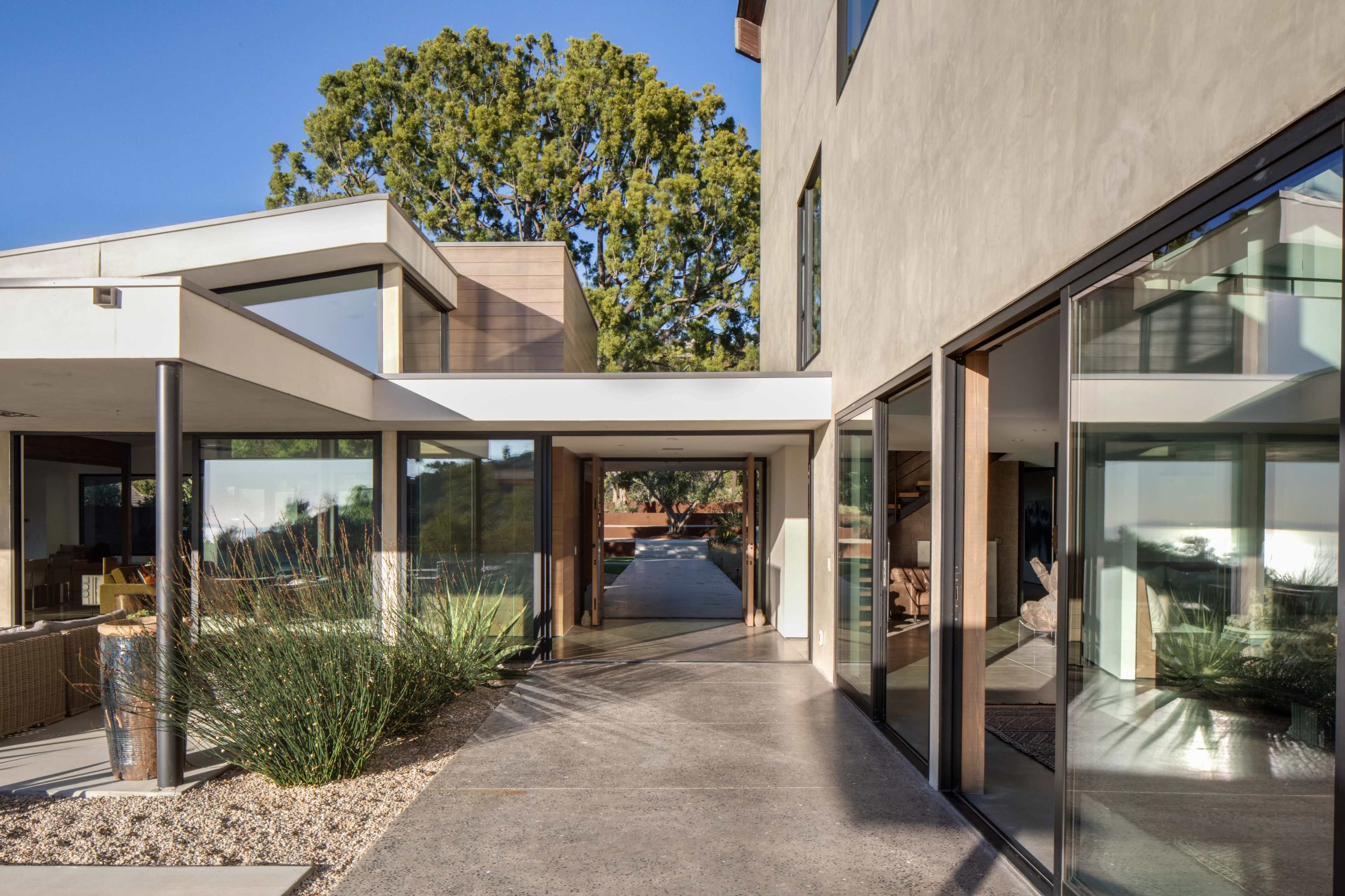 A modern architectural design features a spacious walkway leading through large glass doors toward a lush outdoor area.