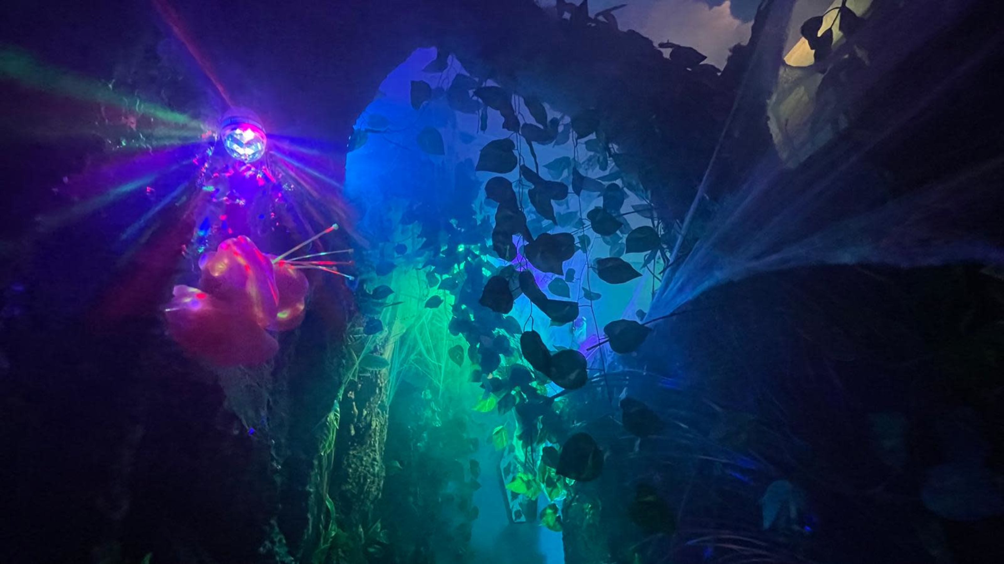 The image shows a dimly lit, colorful jungle scene with illuminated plants and a decorative orb emitting light in various directions.