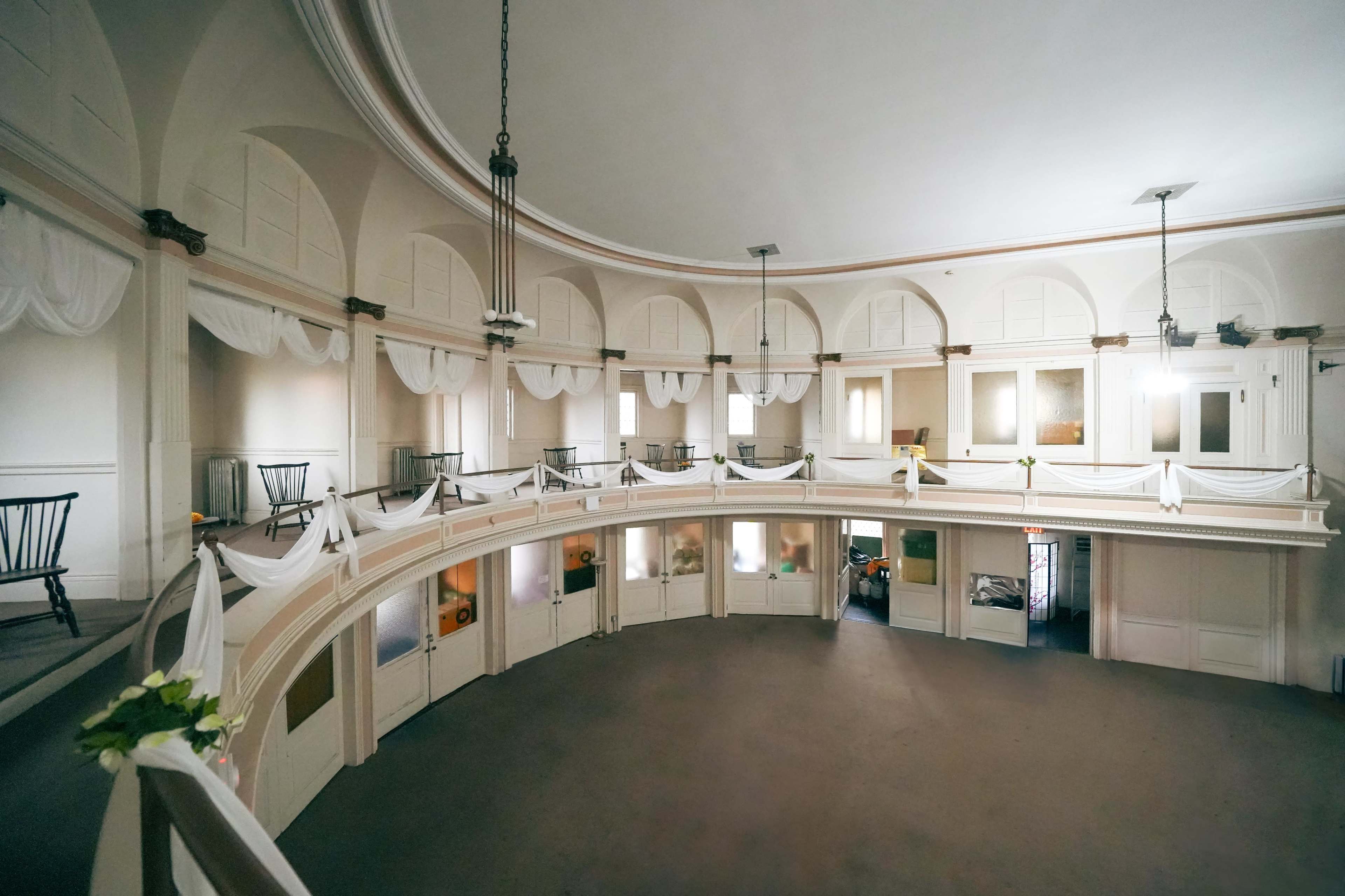 A circular interior space with a balcony, featuring simple chairs and decorative fabric draped along the railings.