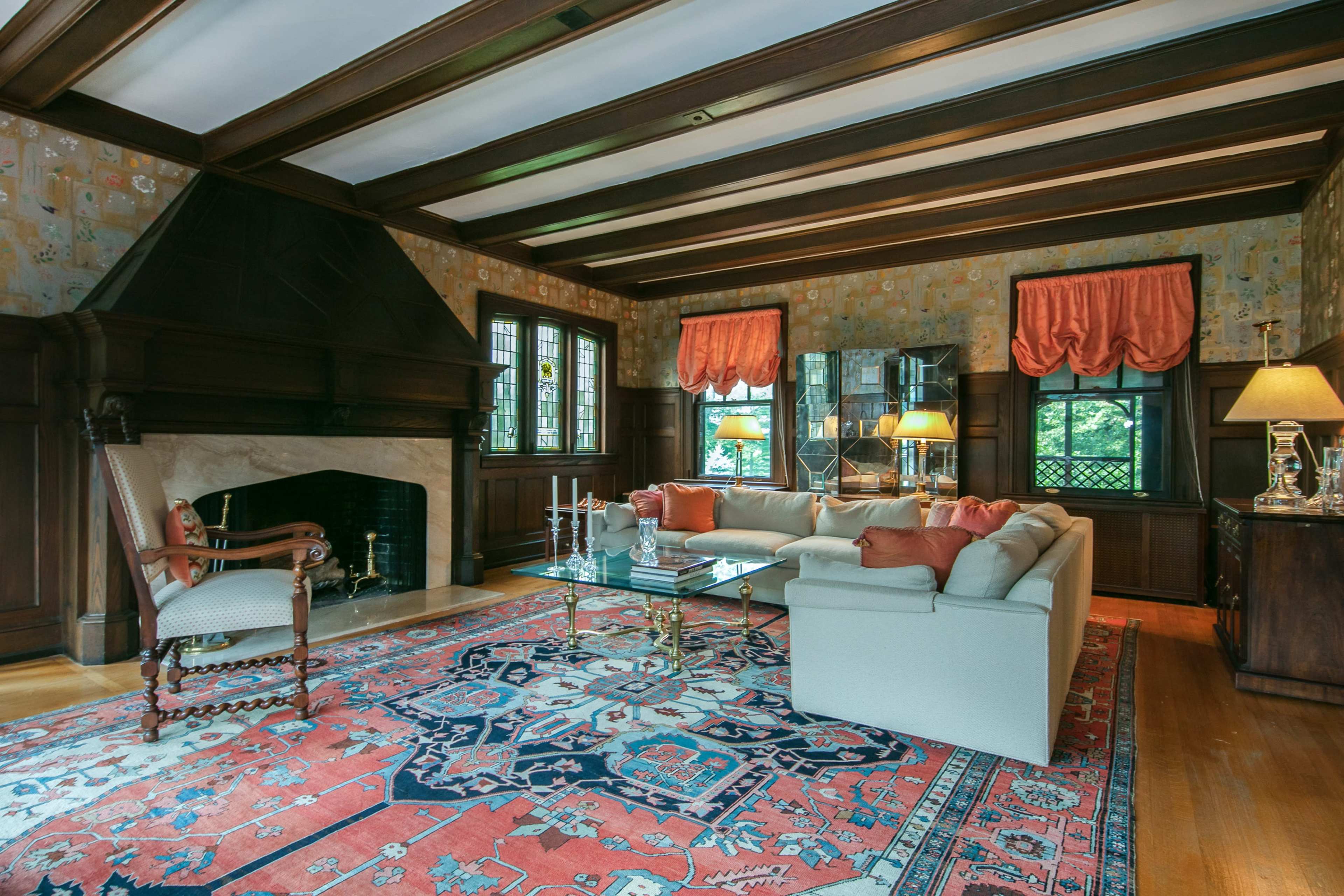 A living room featuring a large rug, a white sofa with cushions, a stone fireplace, and windows adorned with orange drapes.