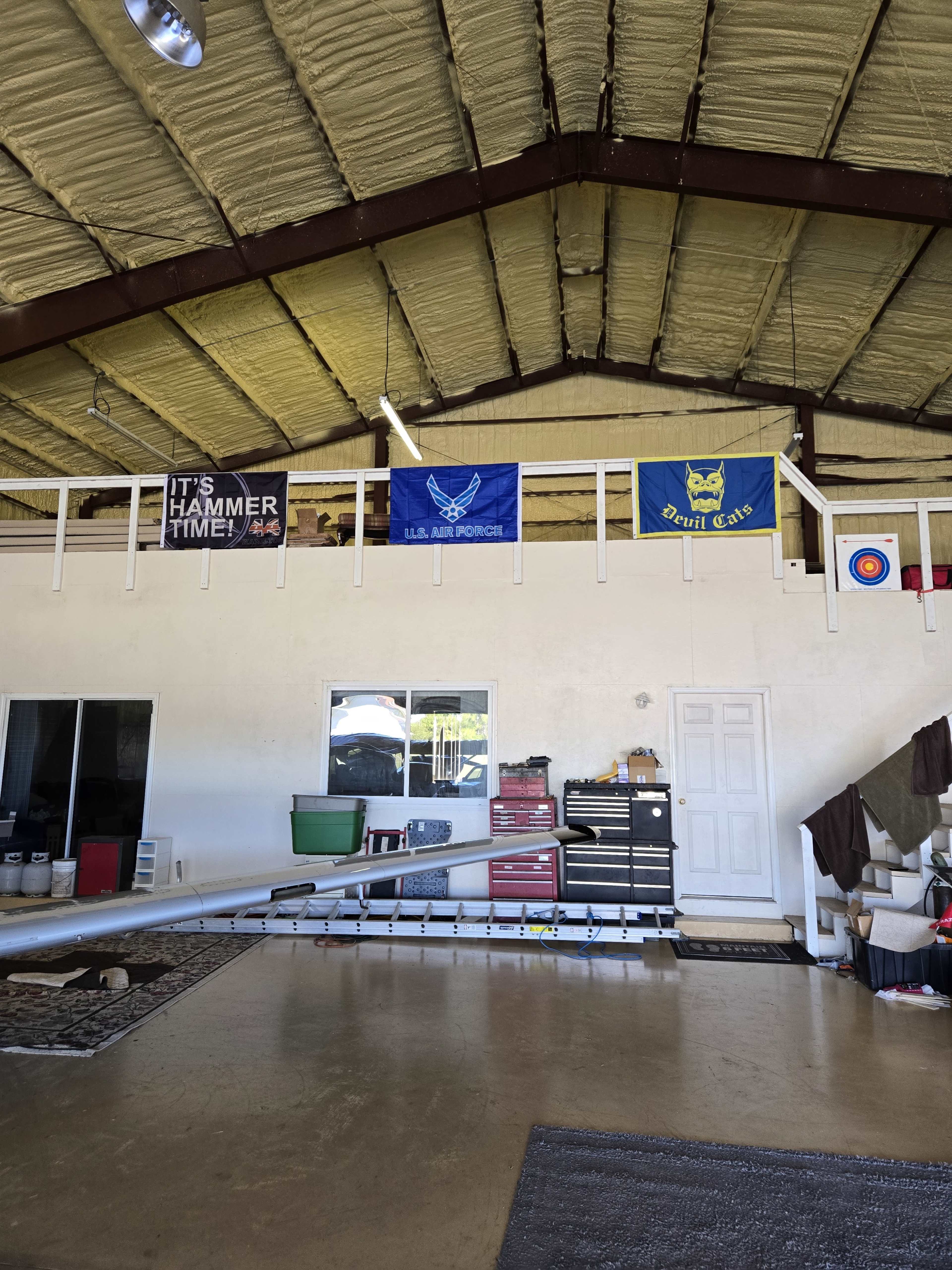 The interior of a building features high ceilings, various flags displayed on a balcony, and tools and equipment arranged on the ground floor.