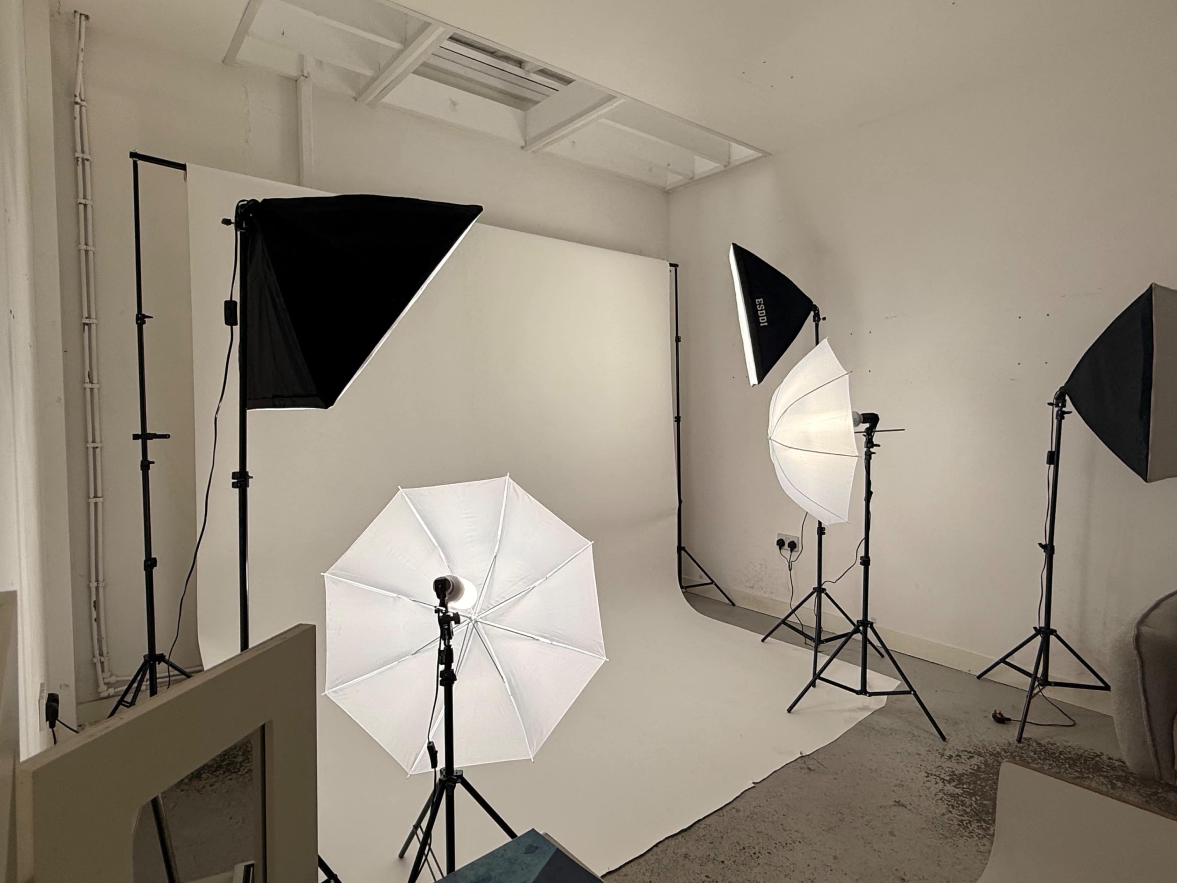 The image shows a photography studio with multiple light setups and a white backdrop.