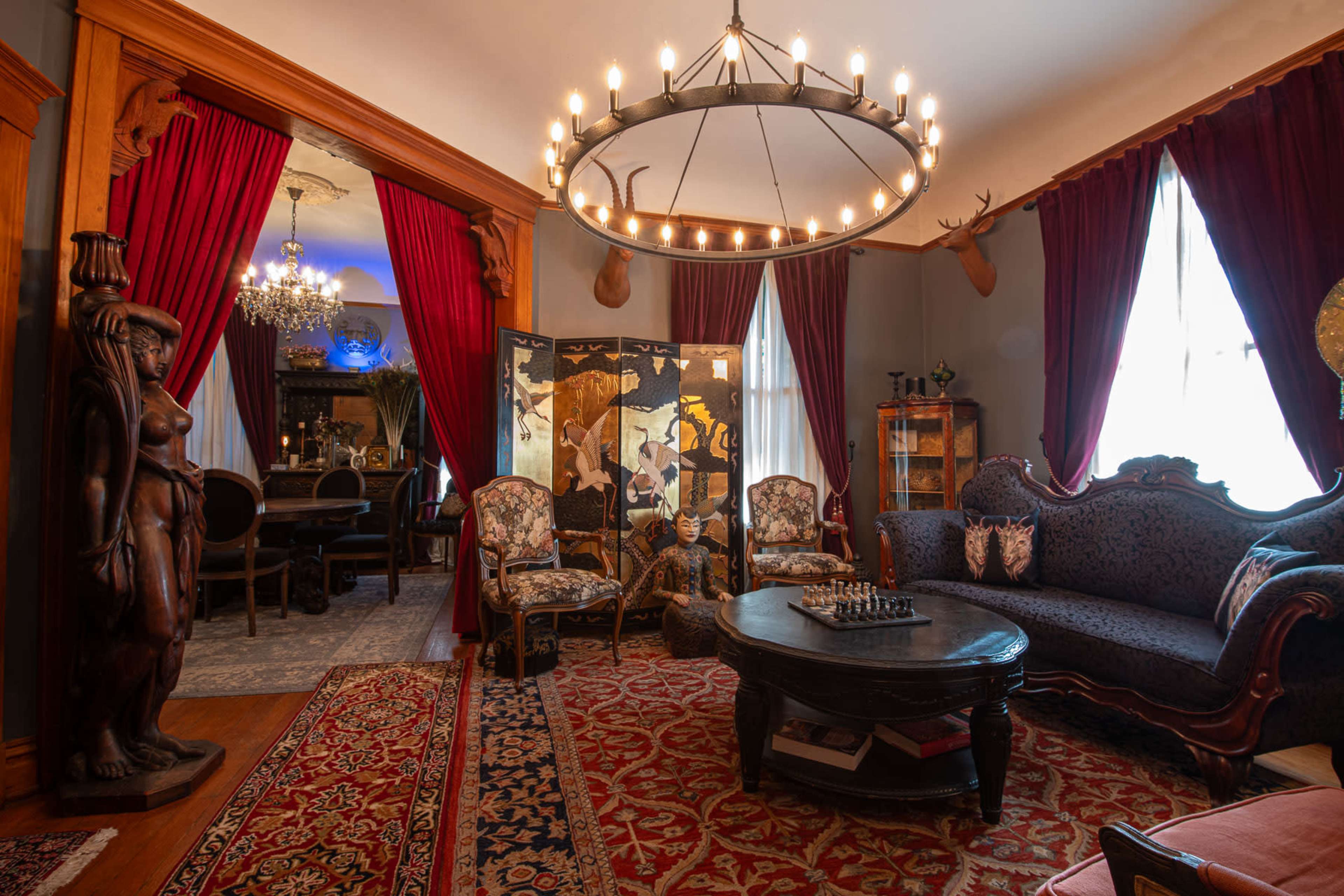 An ornate sitting room with a patterned rug, a large chandelier, velvet curtains, antique furniture, and decorative wall art.