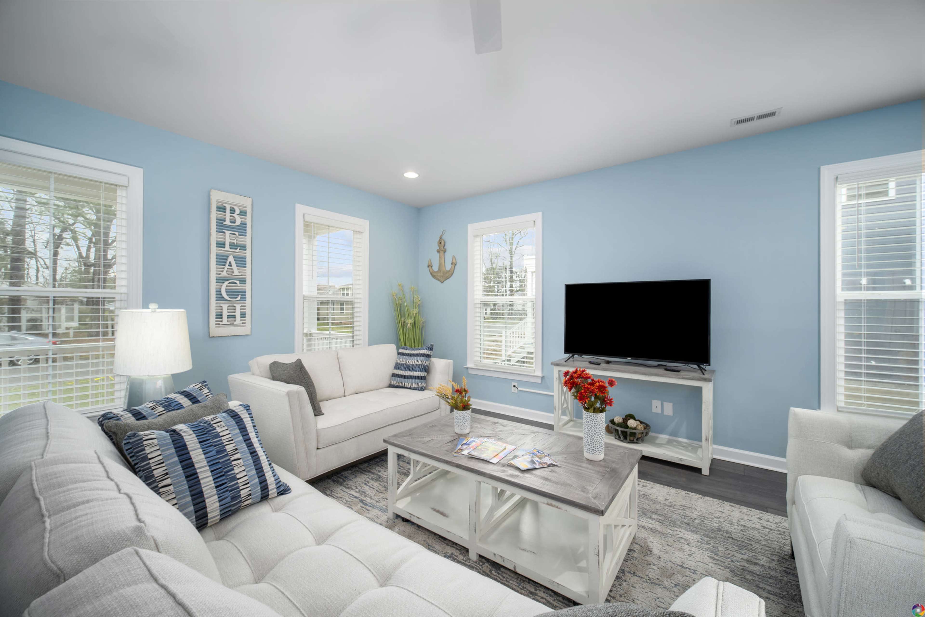 The living room features light blue walls, white furniture, and a television positioned on a white cabinet.