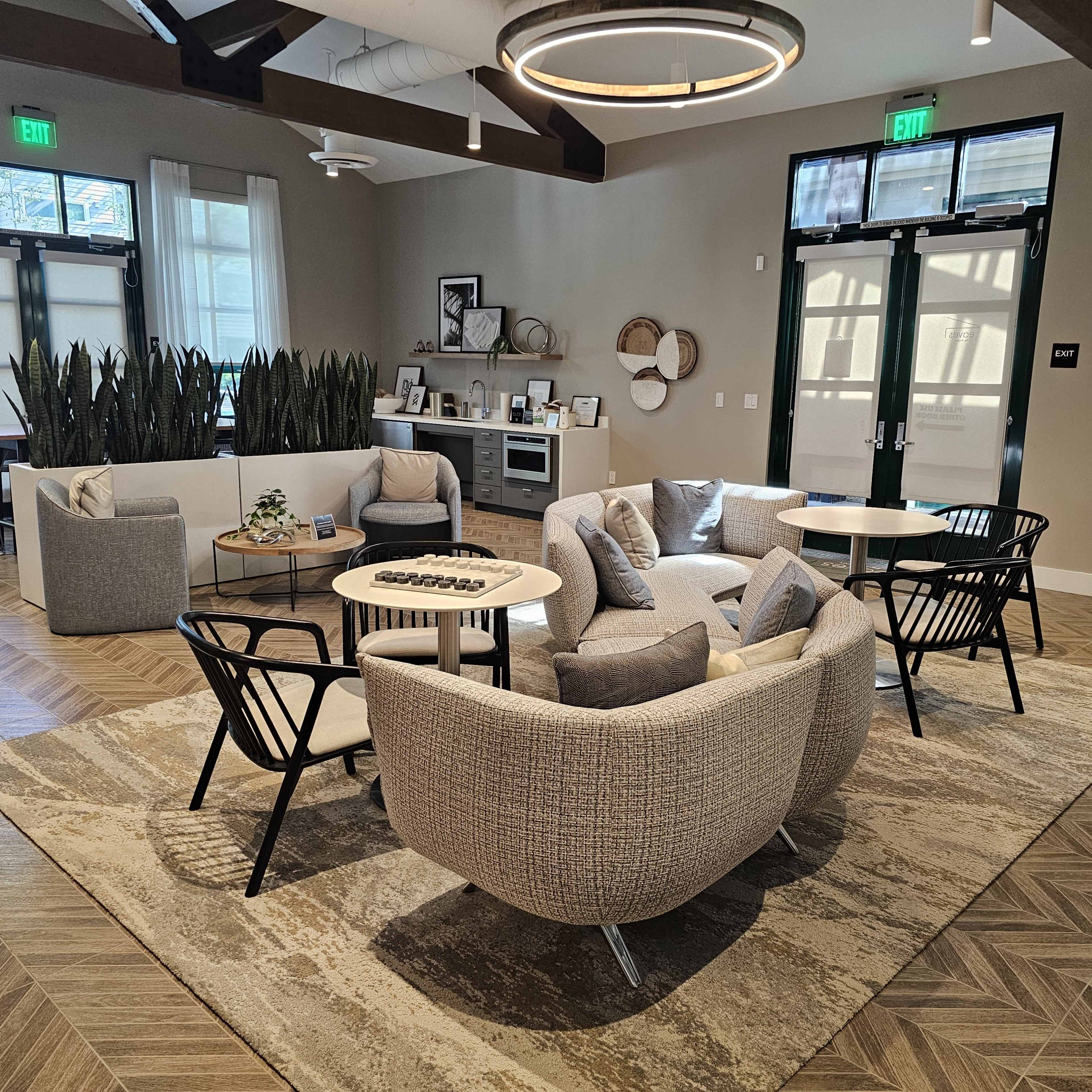 A modern lounge area with various seating options, including plush chairs and sofas, organized around a central table on a patterned rug.