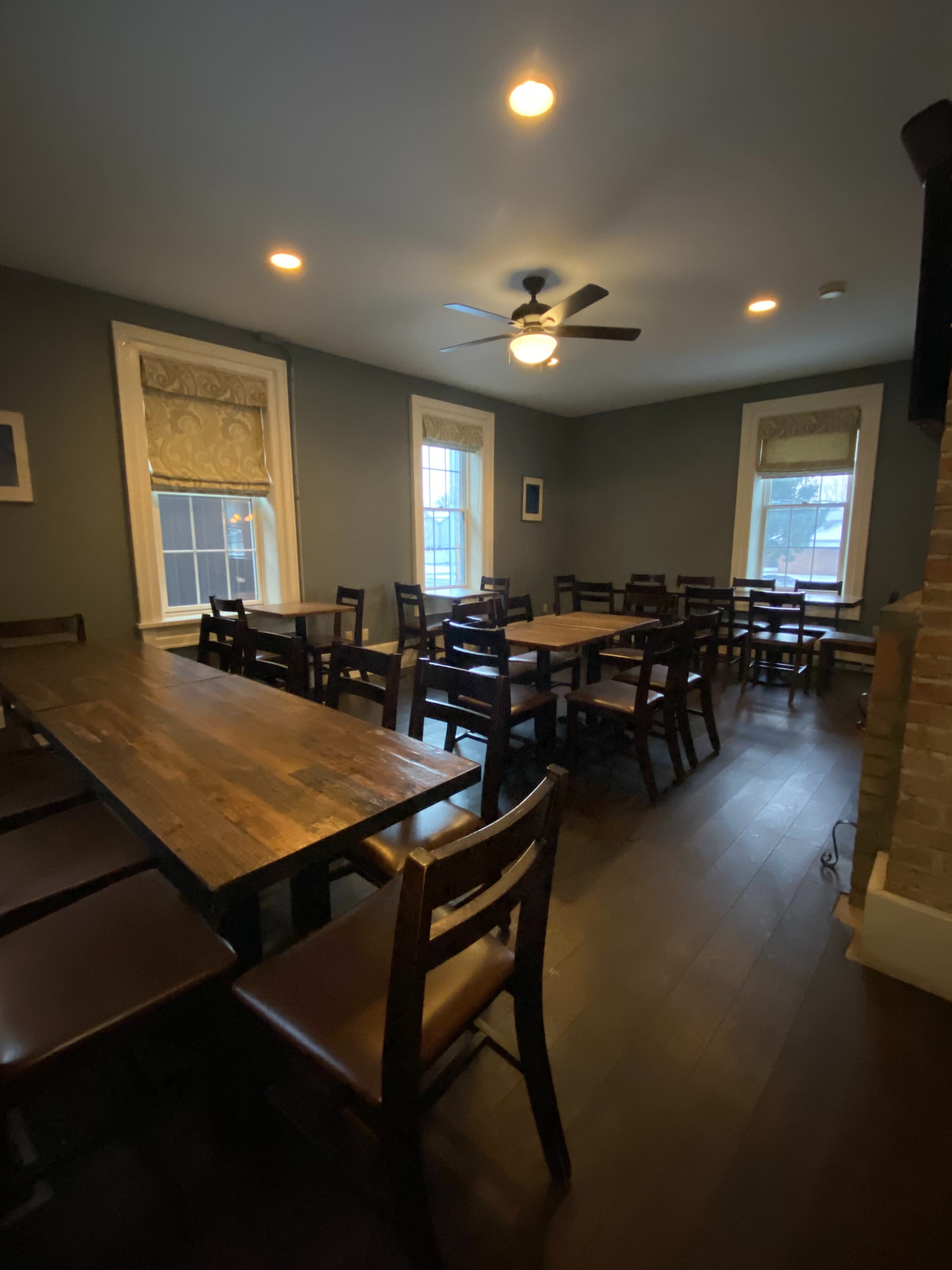 The image shows a dimly lit dining area with several wooden tables and chairs arranged neatly against the walls.
