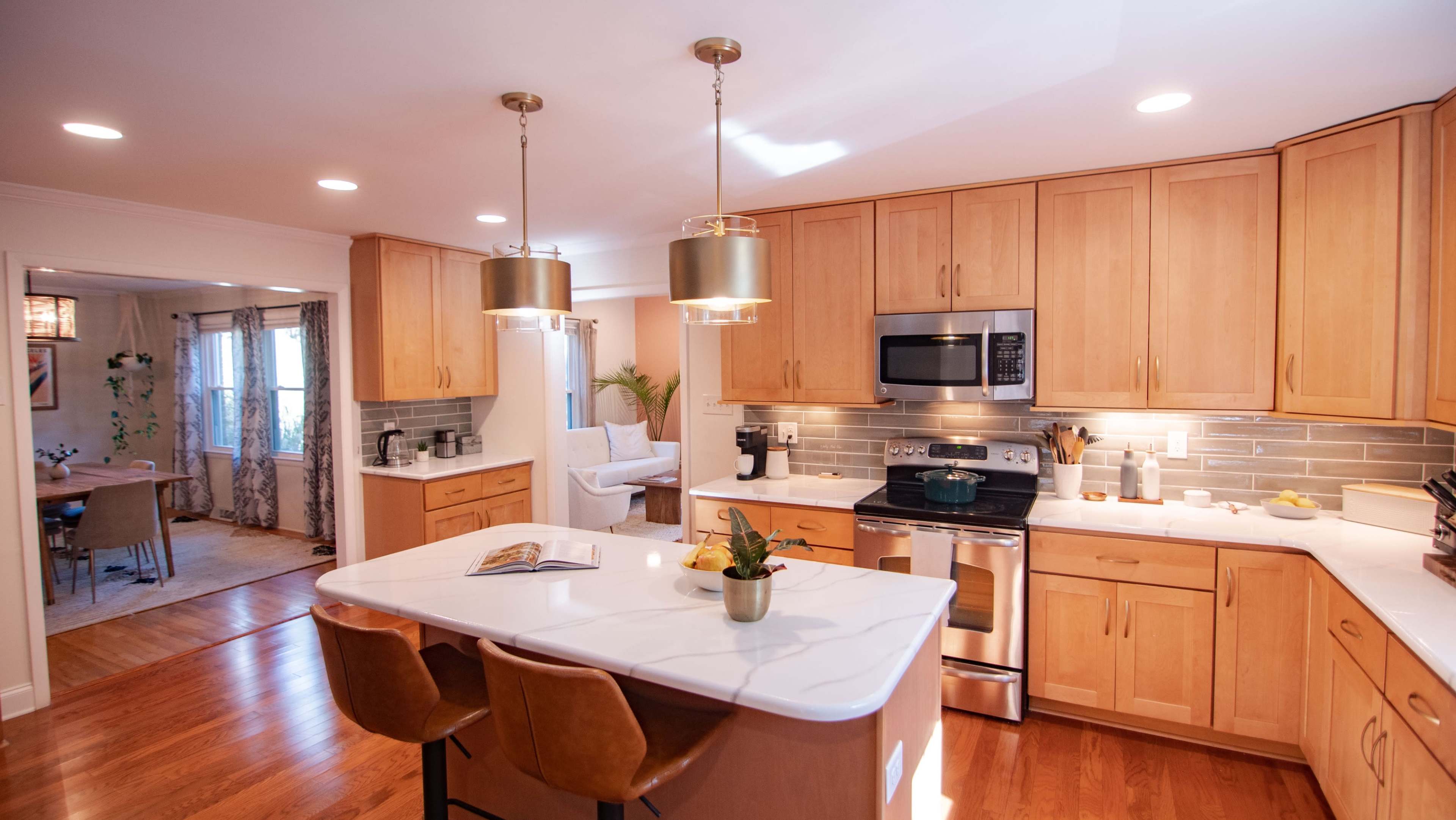 A modern kitchen features wooden cabinetry, stainless steel appliances, and a large island with bar stools and pendant lighting.