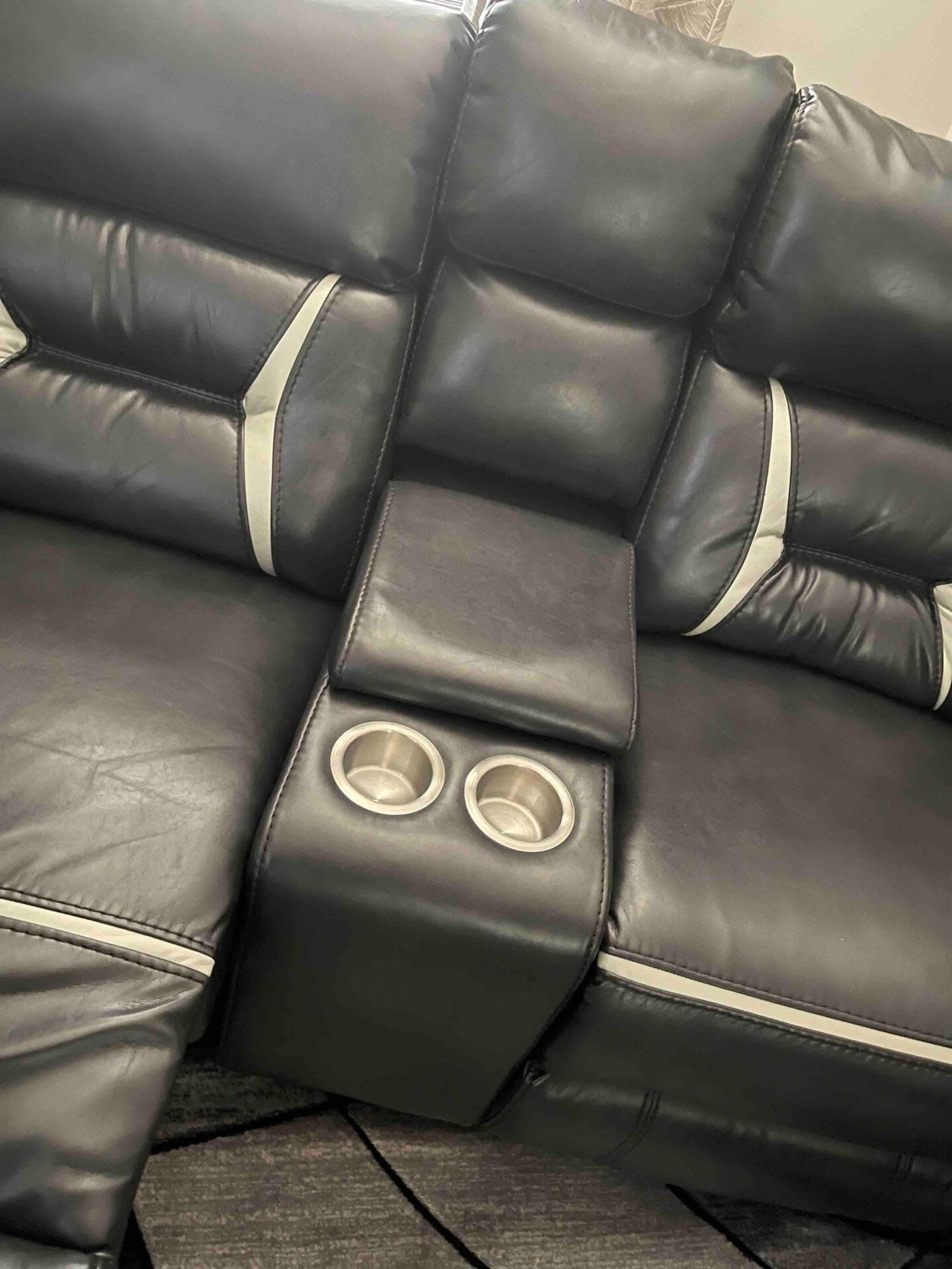 A section of a black leather sofa with a central armrest featuring two cup holders.