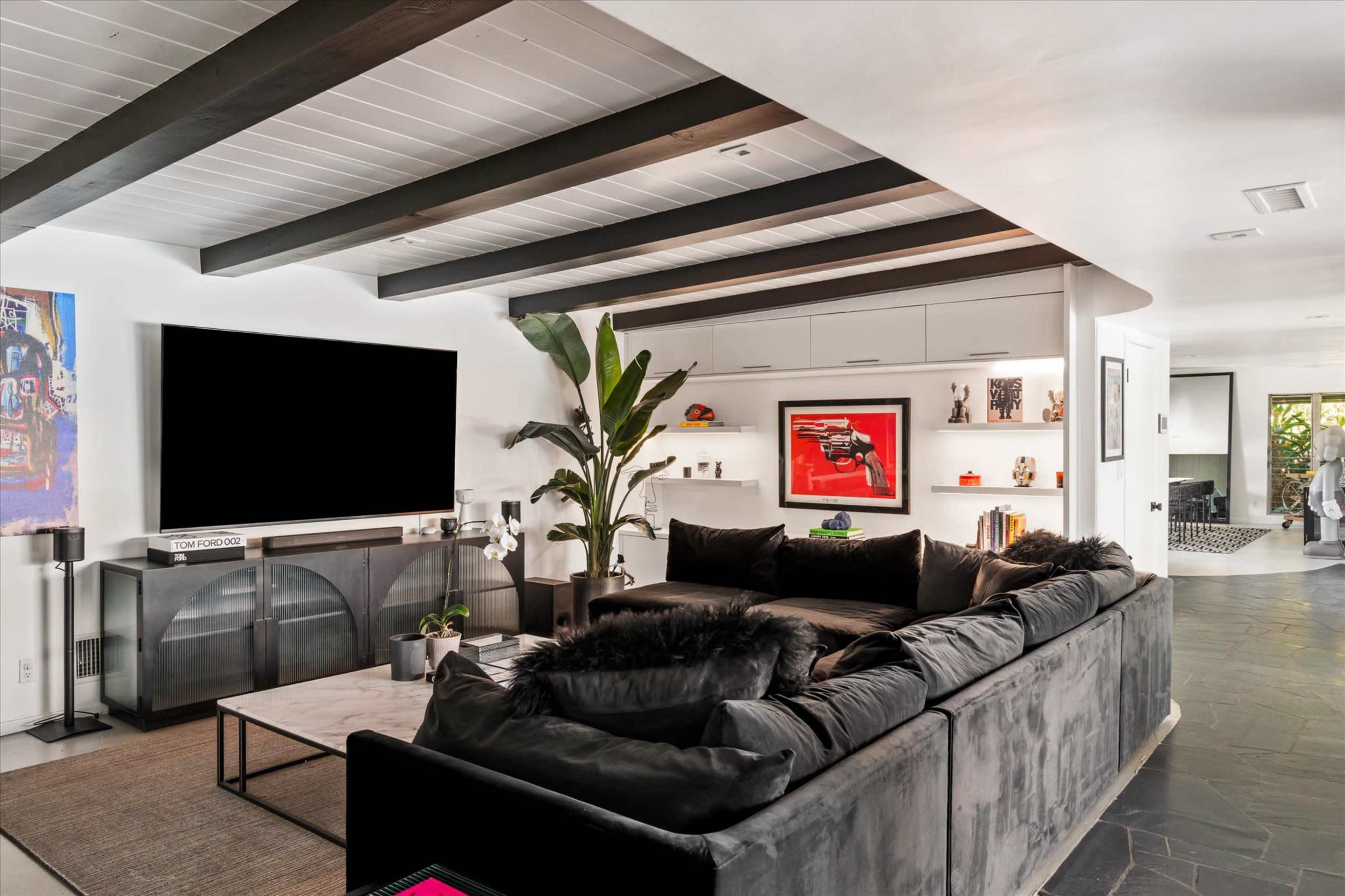 A modern living room features a sectional sofa, a large TV mounted on the wall, and a decorative plant near a sleek coffee table.