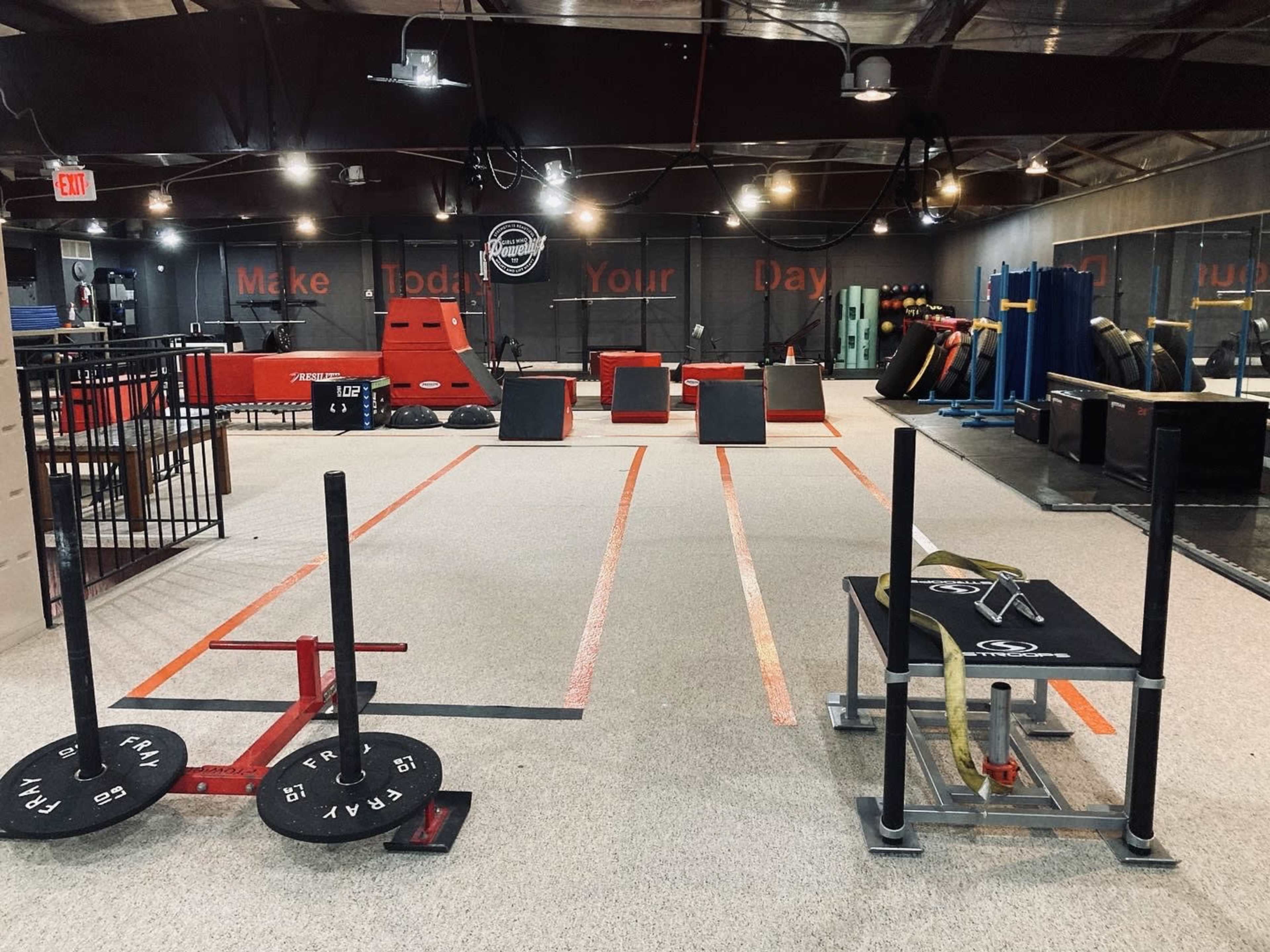 A fitness training facility with various workout equipment including weight plates, sleds, and obstacles arranged on a rubberized floor.