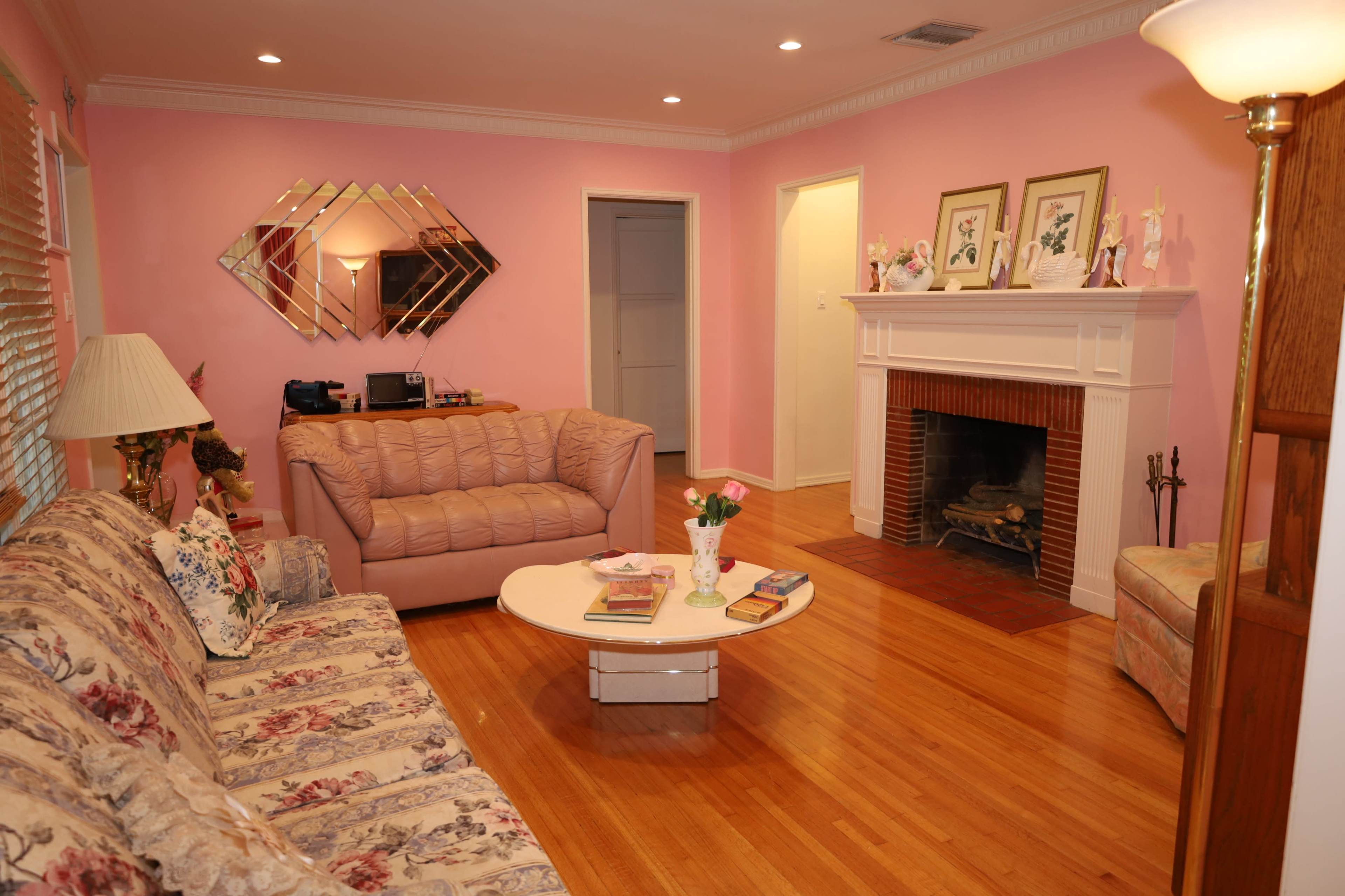 The image shows a cozy living room with pink walls, a fireplace, a coffee table, and a sofa set.