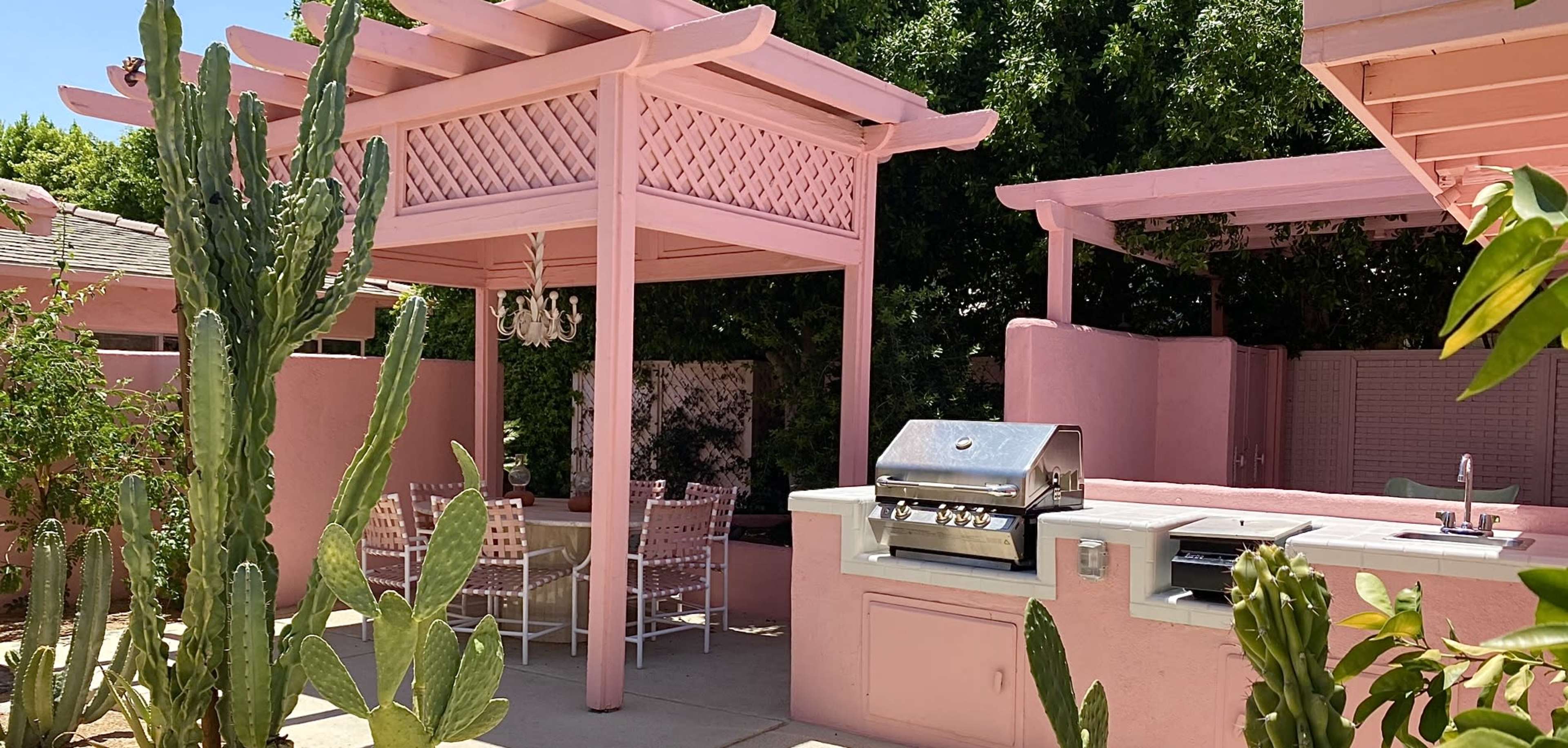 A pink pergola and outdoor kitchen are set in a landscaped area with cacti and seating.