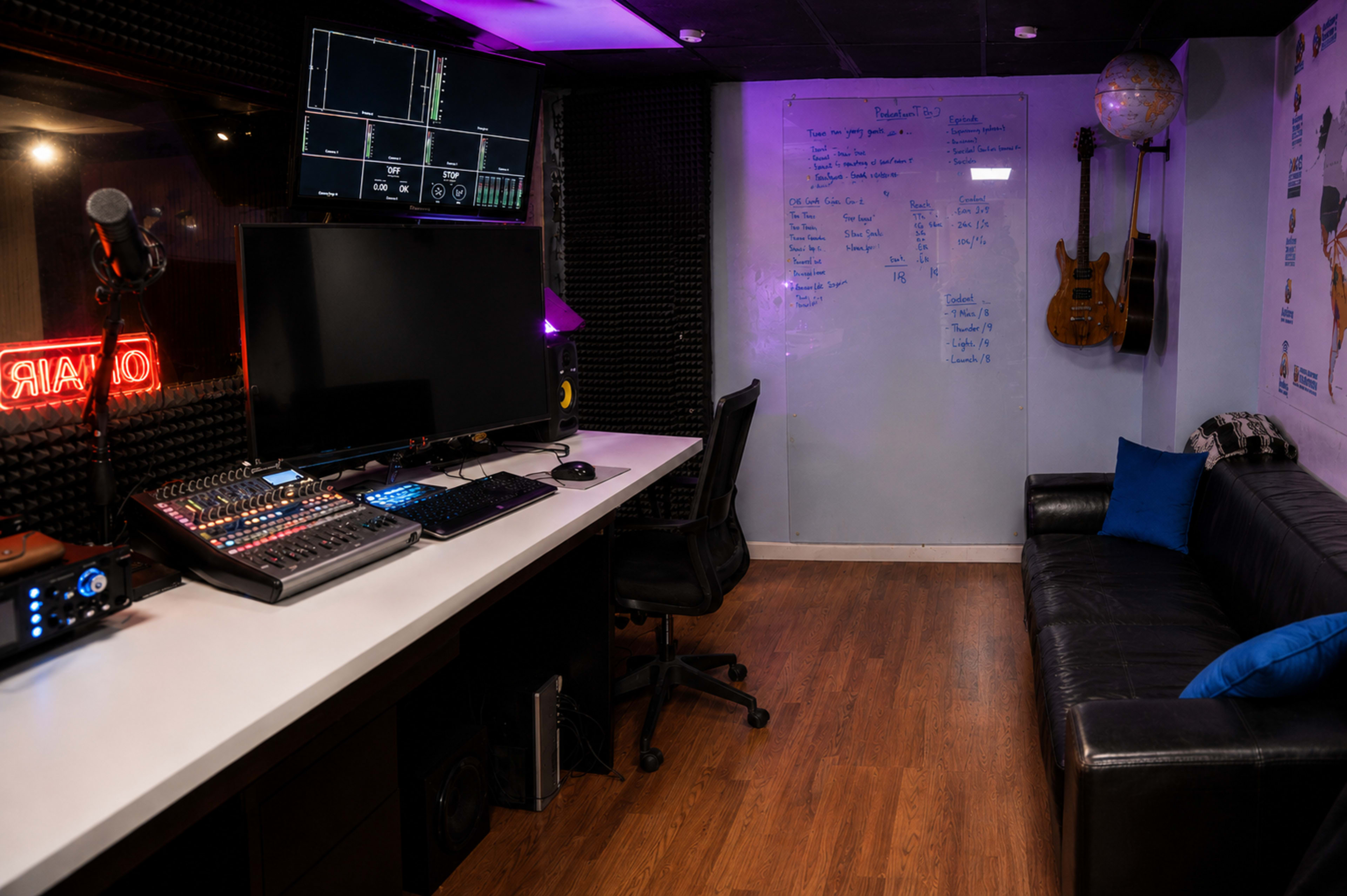The image shows a music studio with a large desk featuring audio equipment, a computer monitor, and a black leather couch against the wall.