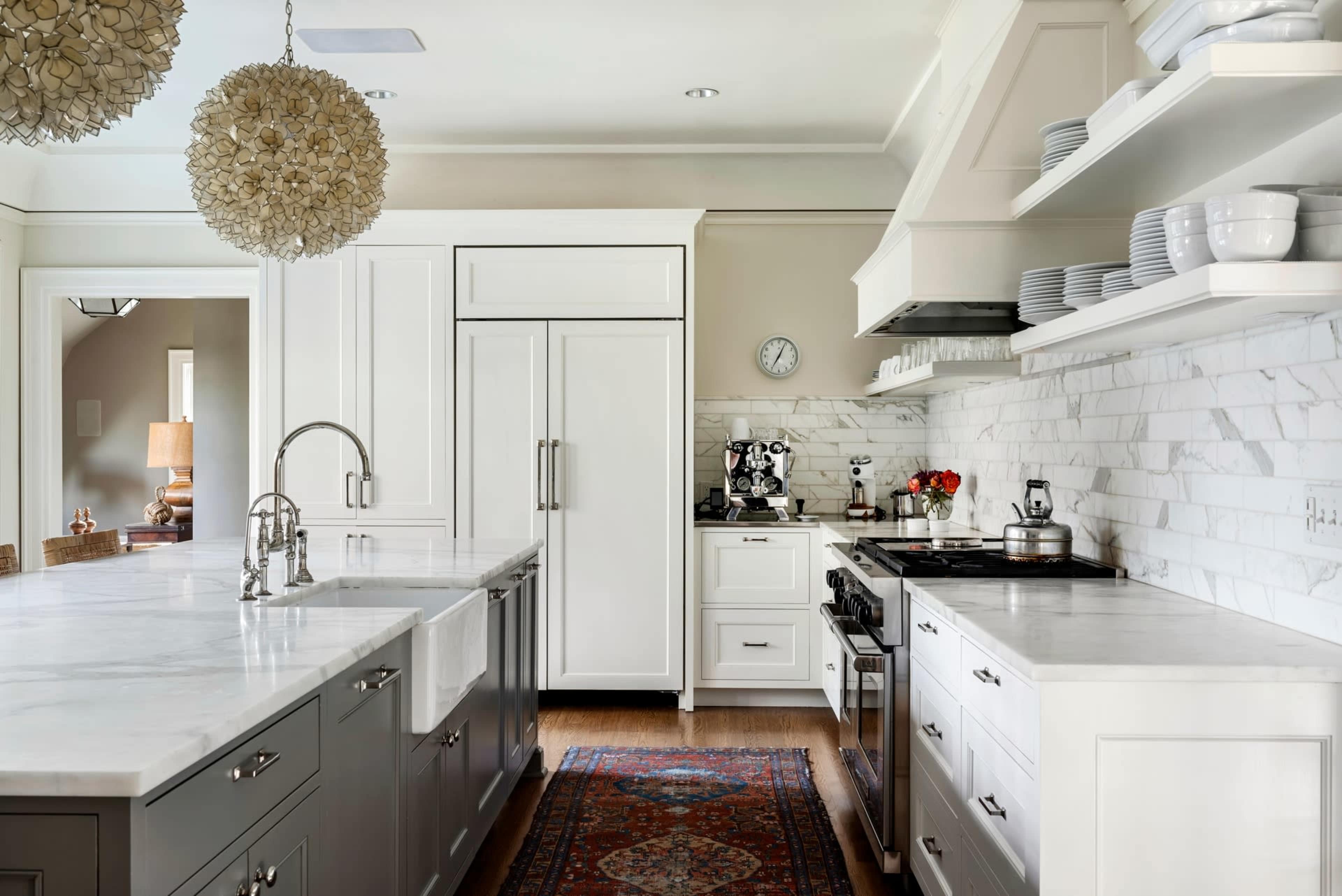 The kitchen features white cabinetry, marble countertops, stainless steel appliances, and an area rug on wooden flooring.
