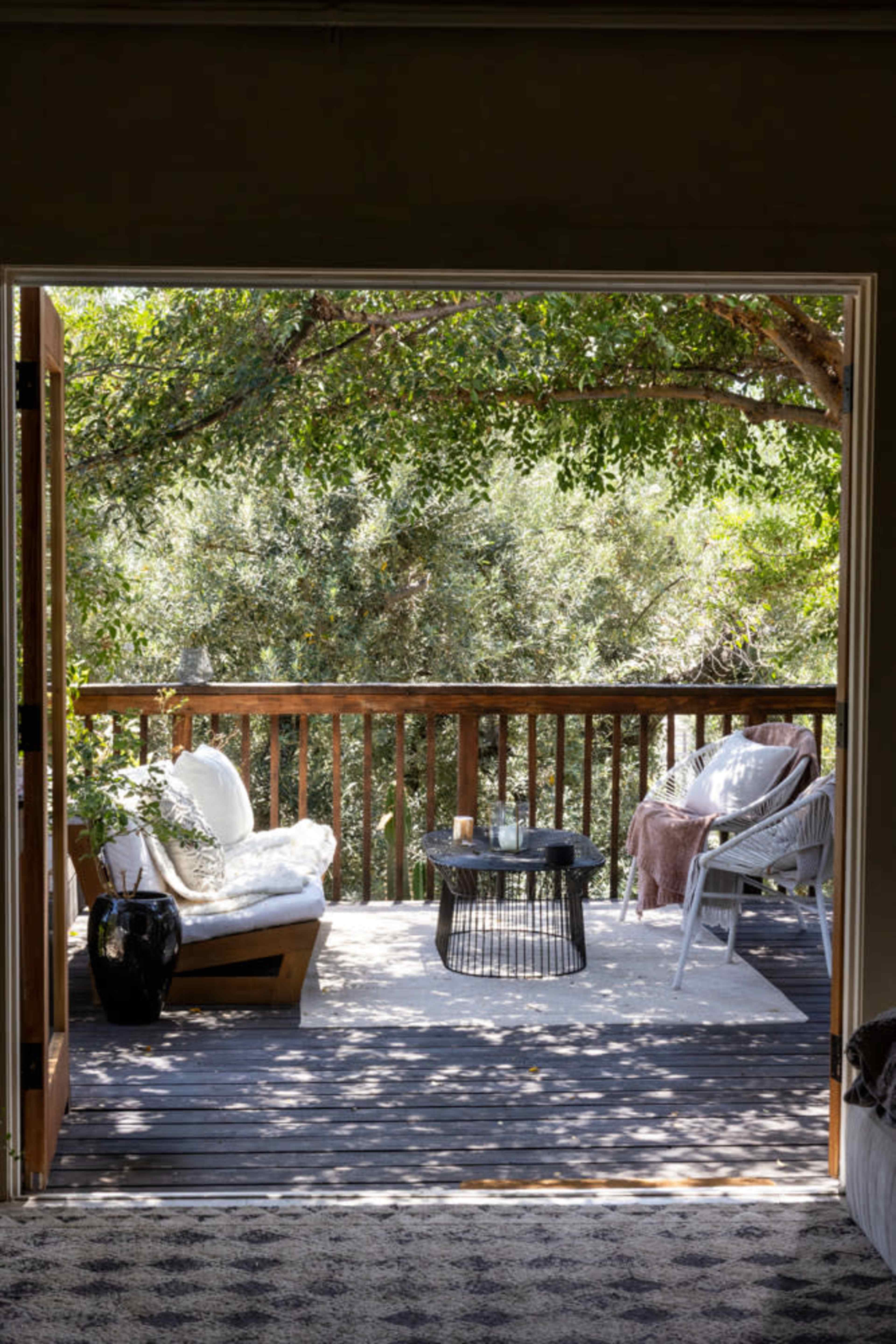 A well-furnished outdoor deck features comfortable seating and a small table, surrounded by lush greenery.
