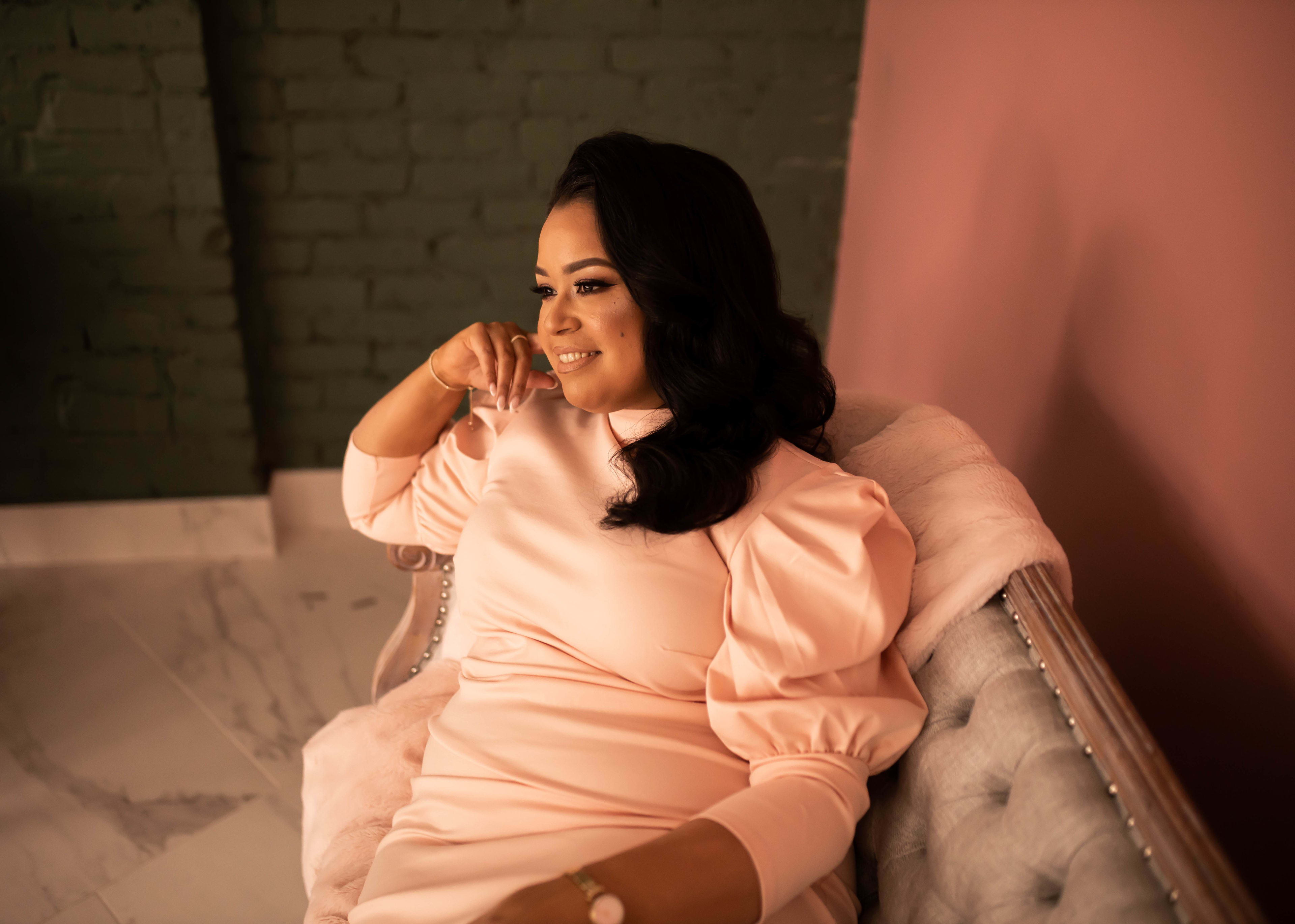 A photoshoot of a woman in a pink dress sitting in a chair.