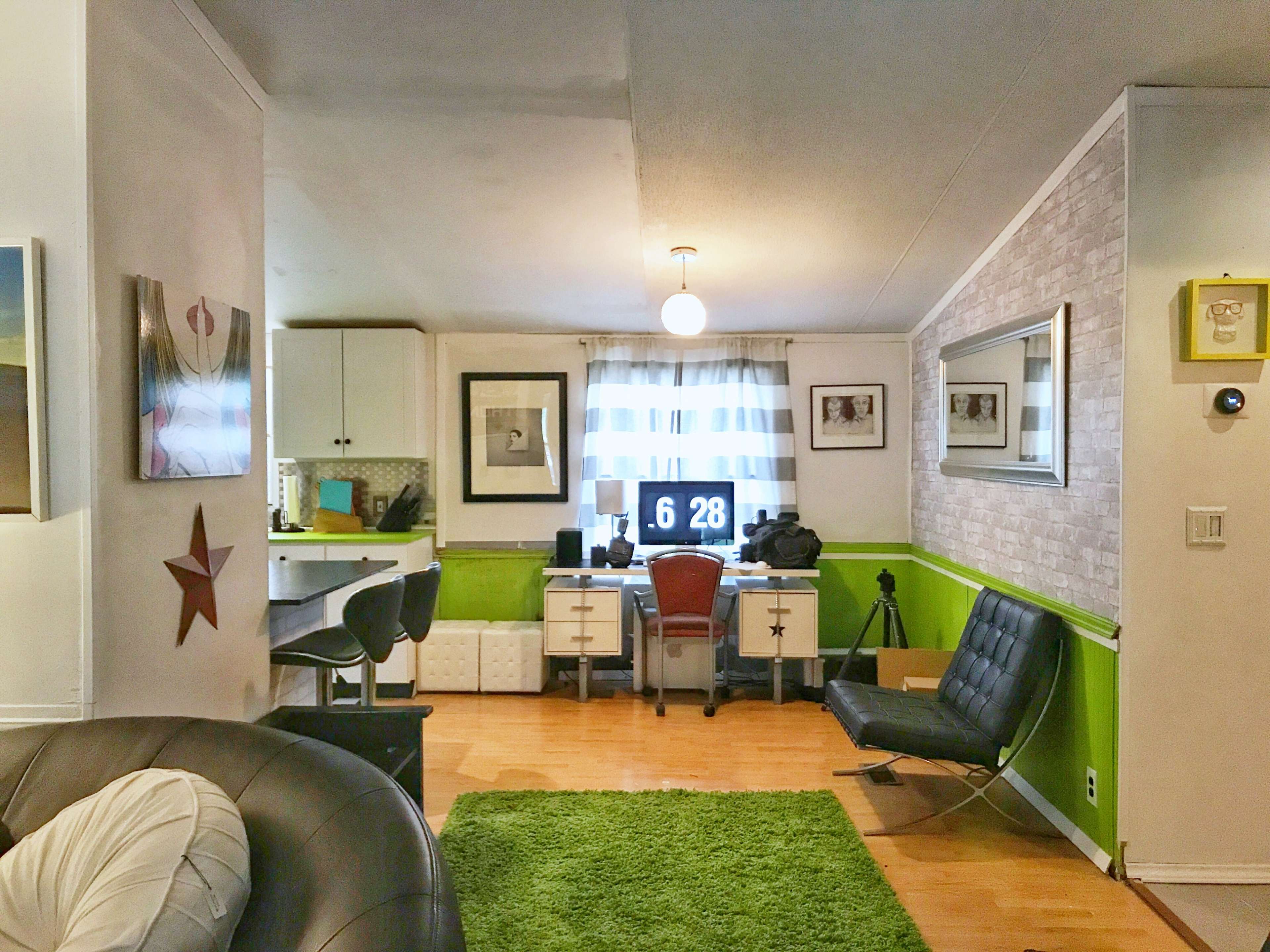 A modern living area with a workspace featuring a desk, computer, and various decorations, along with a green accent wall and a seating area with a black chair.