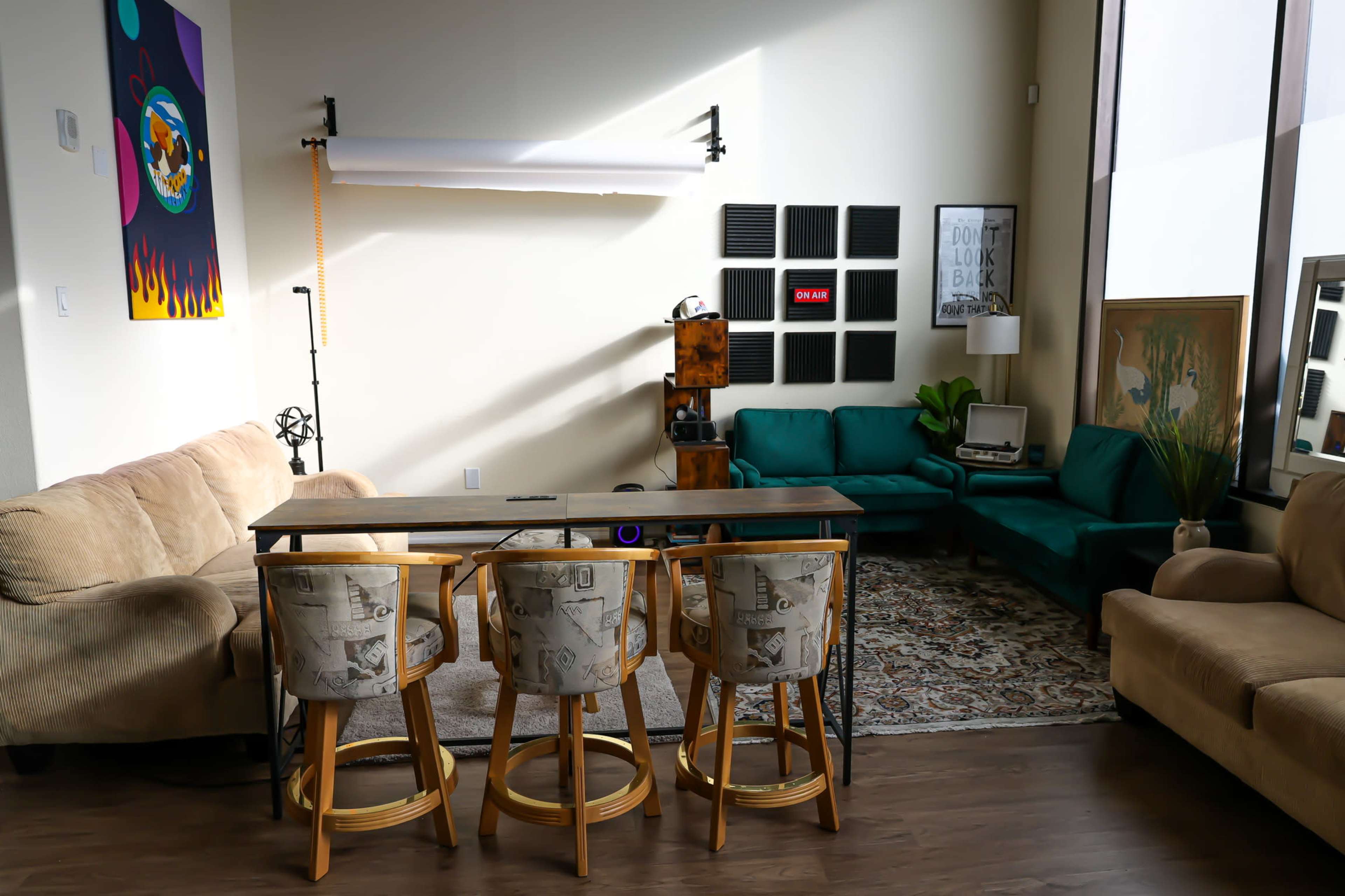 The image shows a modern living area with a green couch, beige chairs around a table, and decorative elements on the walls, including a large photo backdrop and artwork.