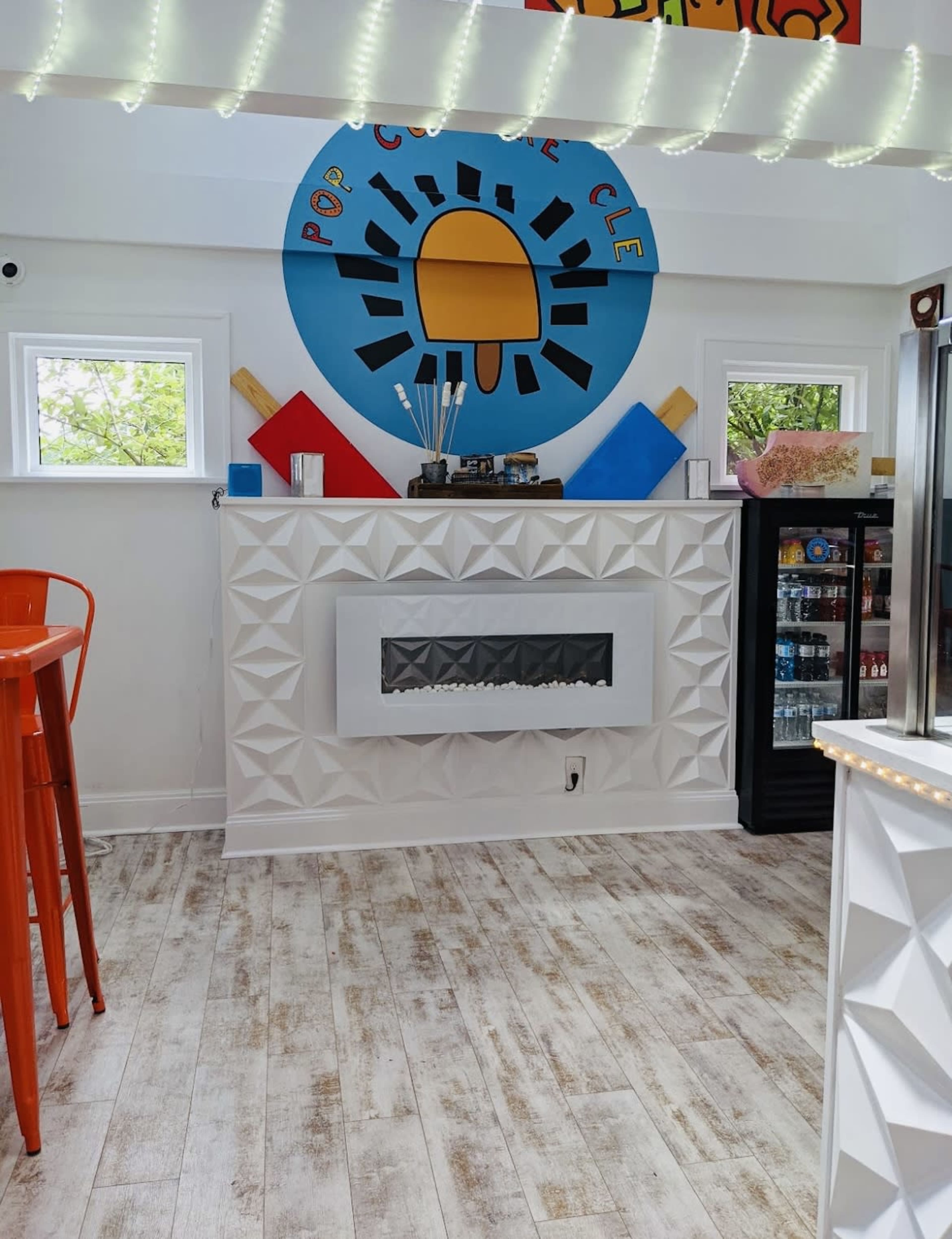 A modern interior of an ice cream shop featuring a decorative wall with a sun logo, a geometric white fireplace, and colorful accents in the decor.
