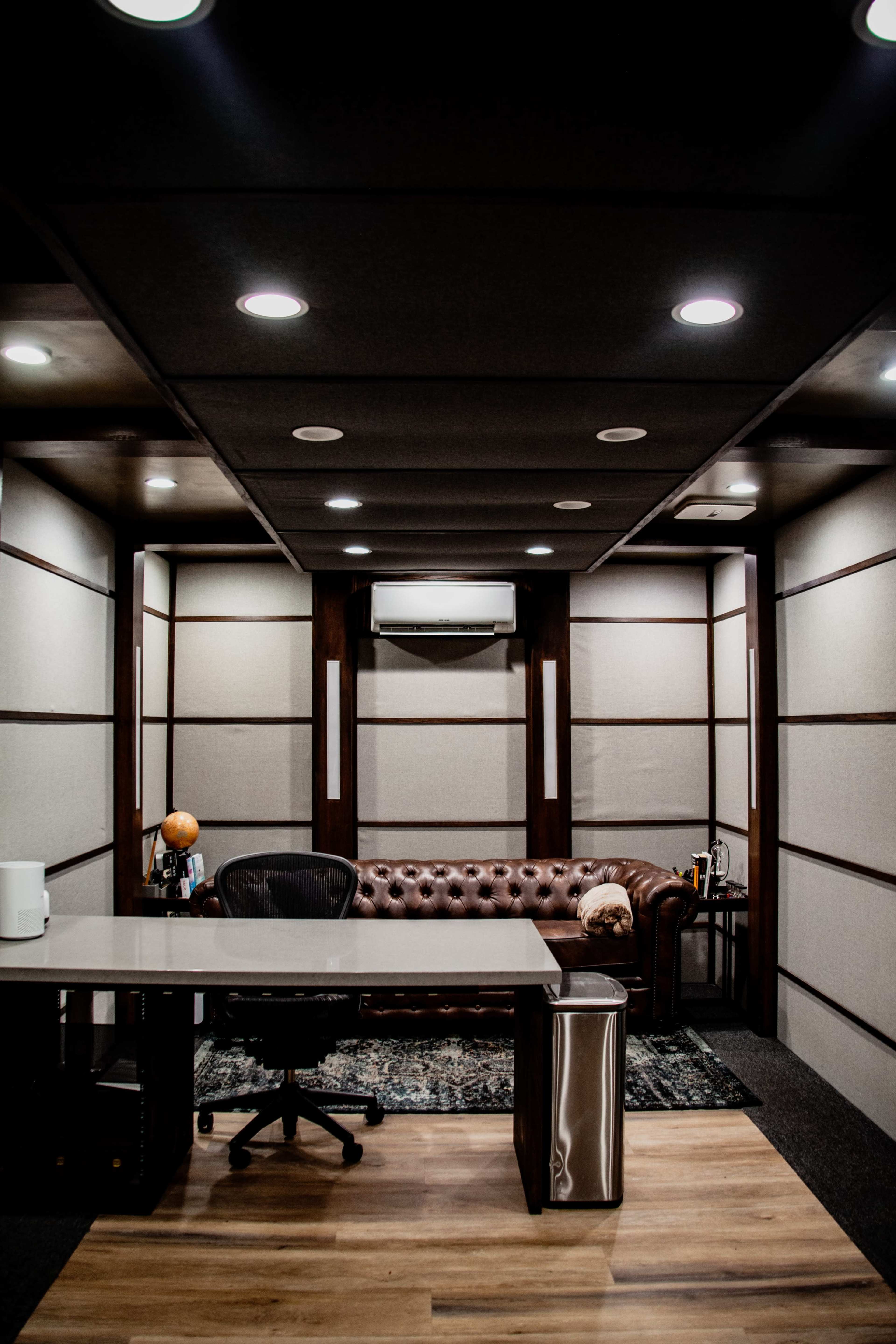 A modern office space featuring a leather sofa, a large desk with a rolling chair, and a decorative globe, all set against panelled walls and ceiling lights.