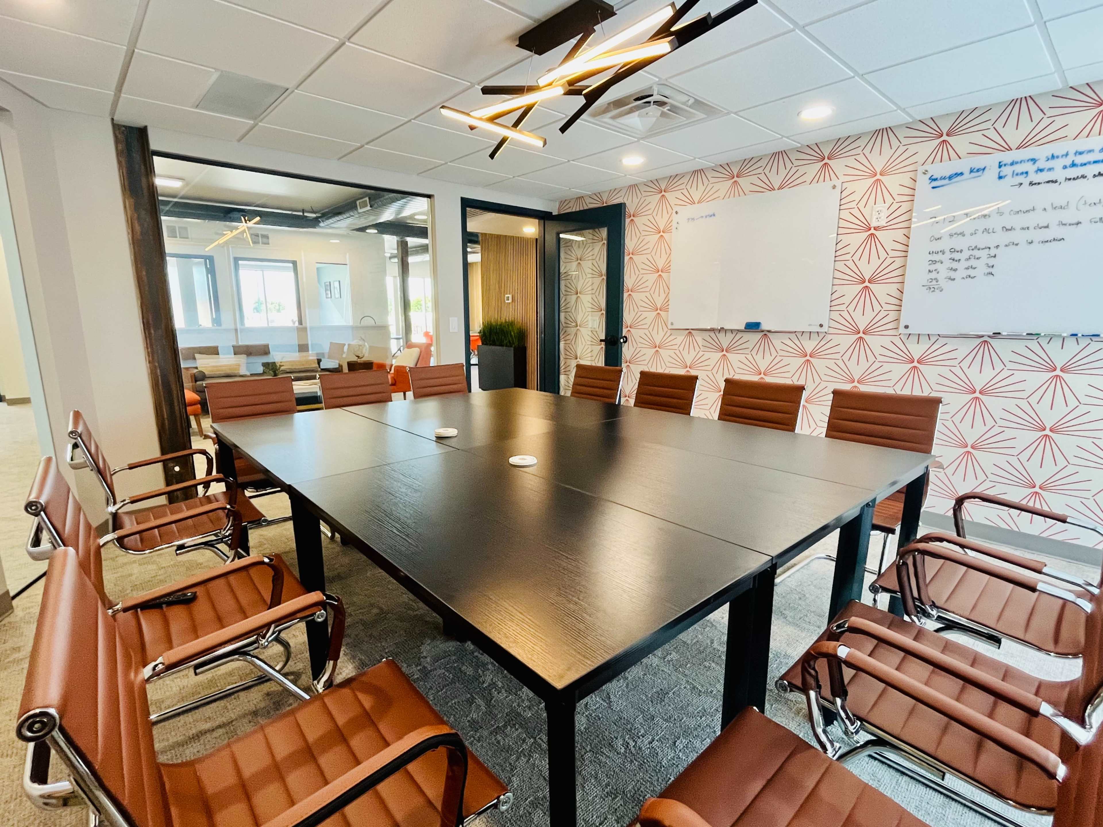 A modern conference room with a large black table surrounded by brown leather chairs, a whiteboard, and patterned wallpaper.