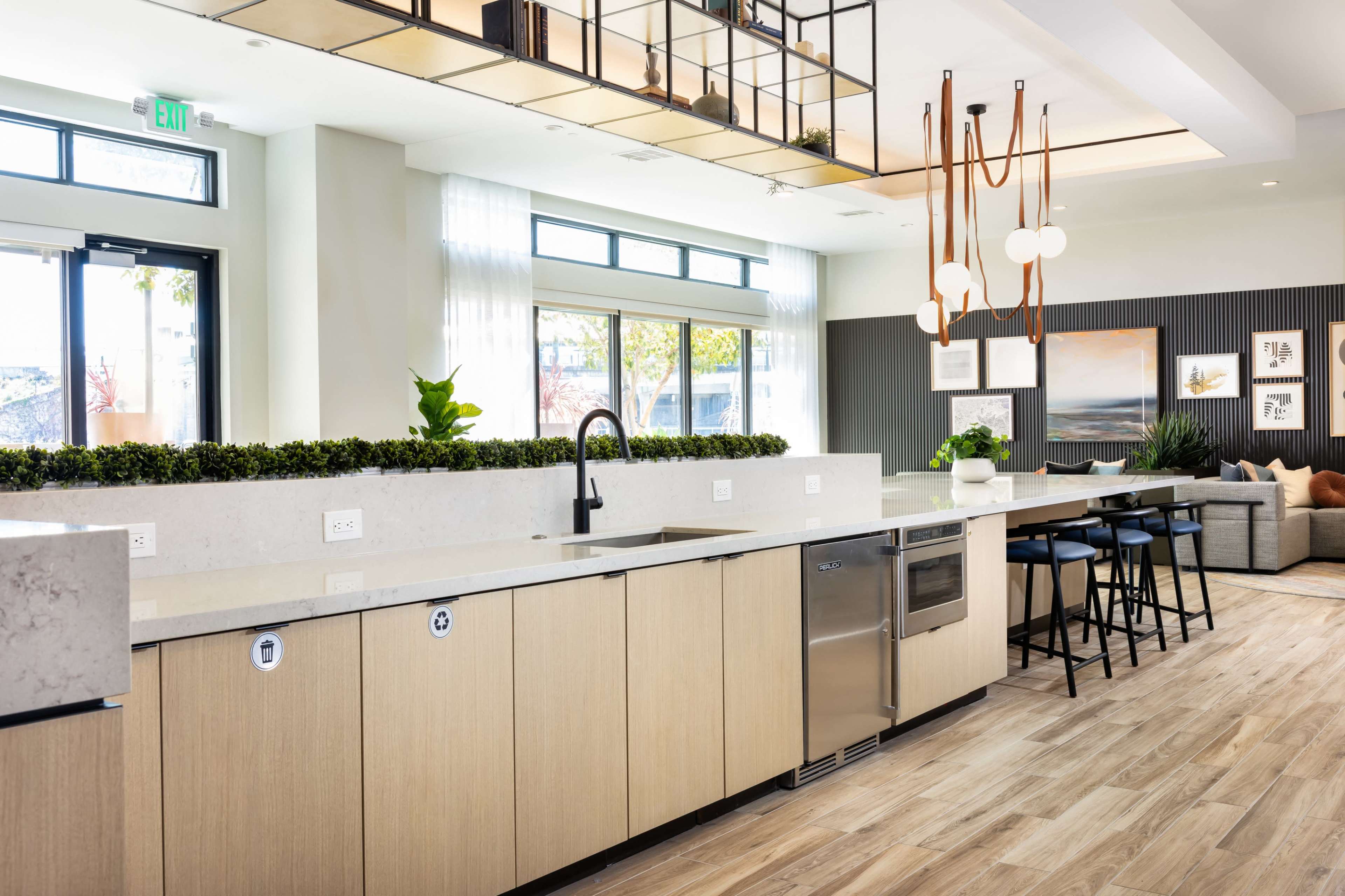 The image shows a modern kitchen with a long countertop, stainless steel appliances, and a spacious seating area with bar stools.