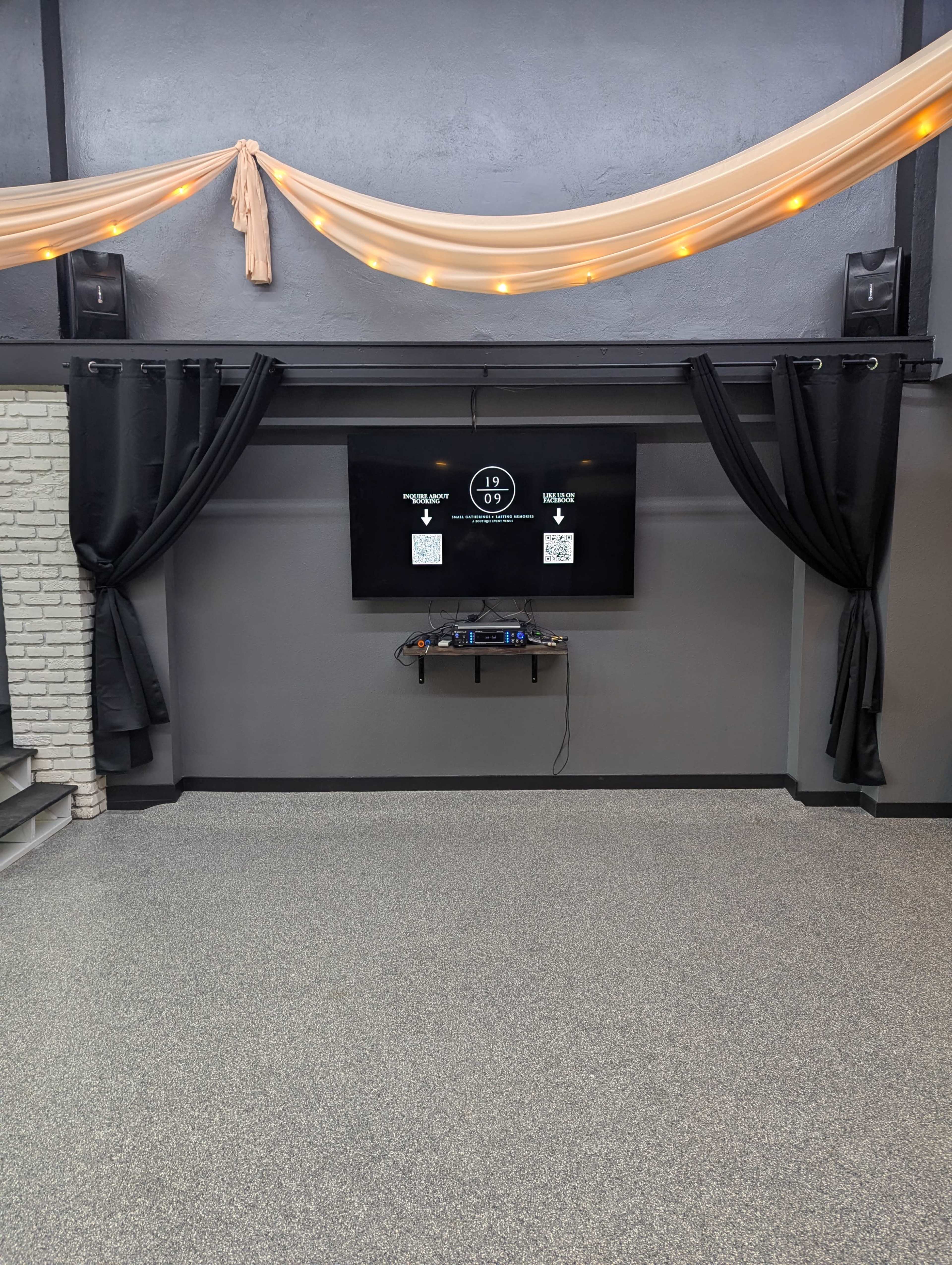 The image shows a room with gray walls, a large black TV mounted on the wall, and curtains framing the TV, along with decorative fabric draped from the ceiling.