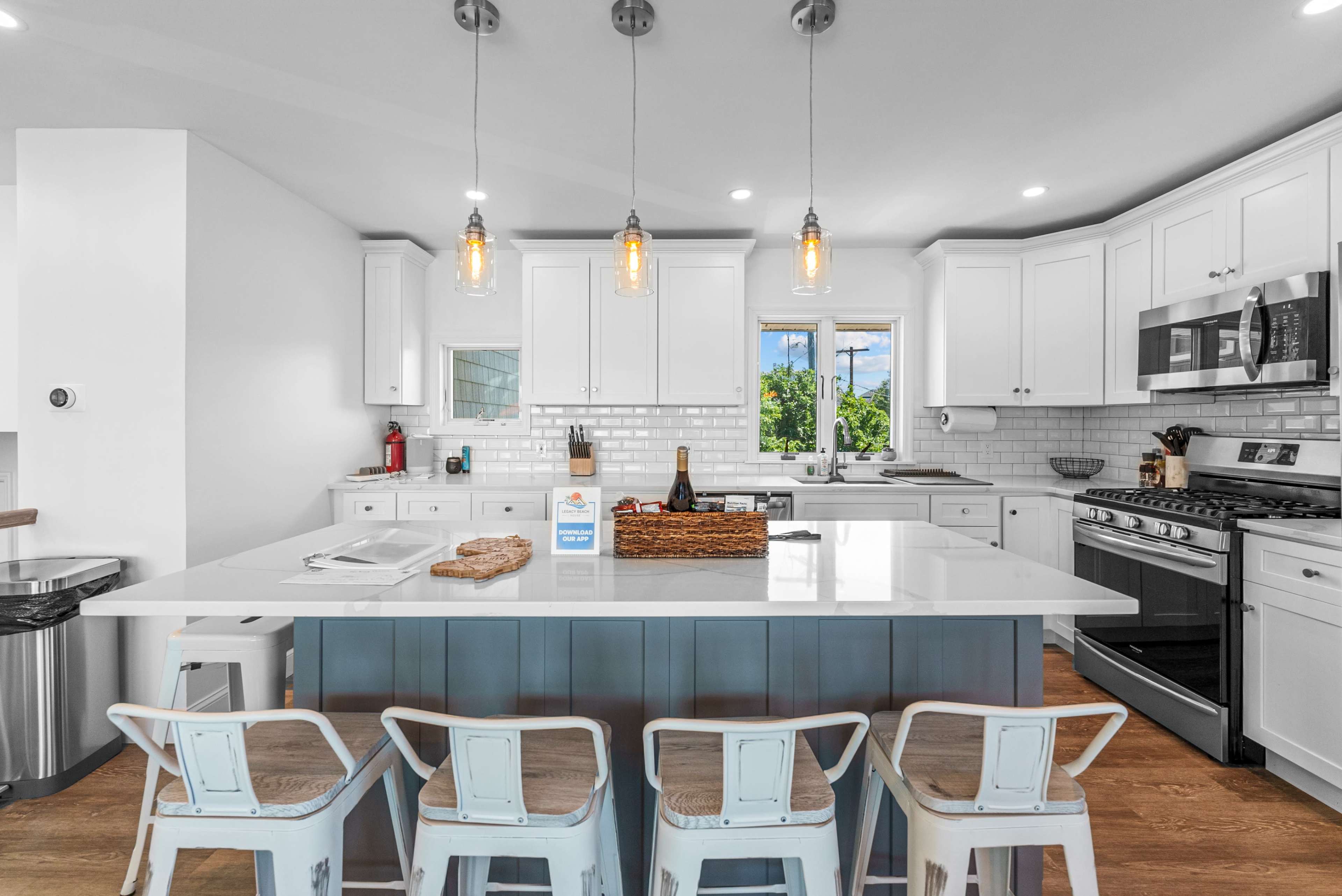 A modern kitchen features white cabinetry, a large island with bar seating, and windows that provide natural light.