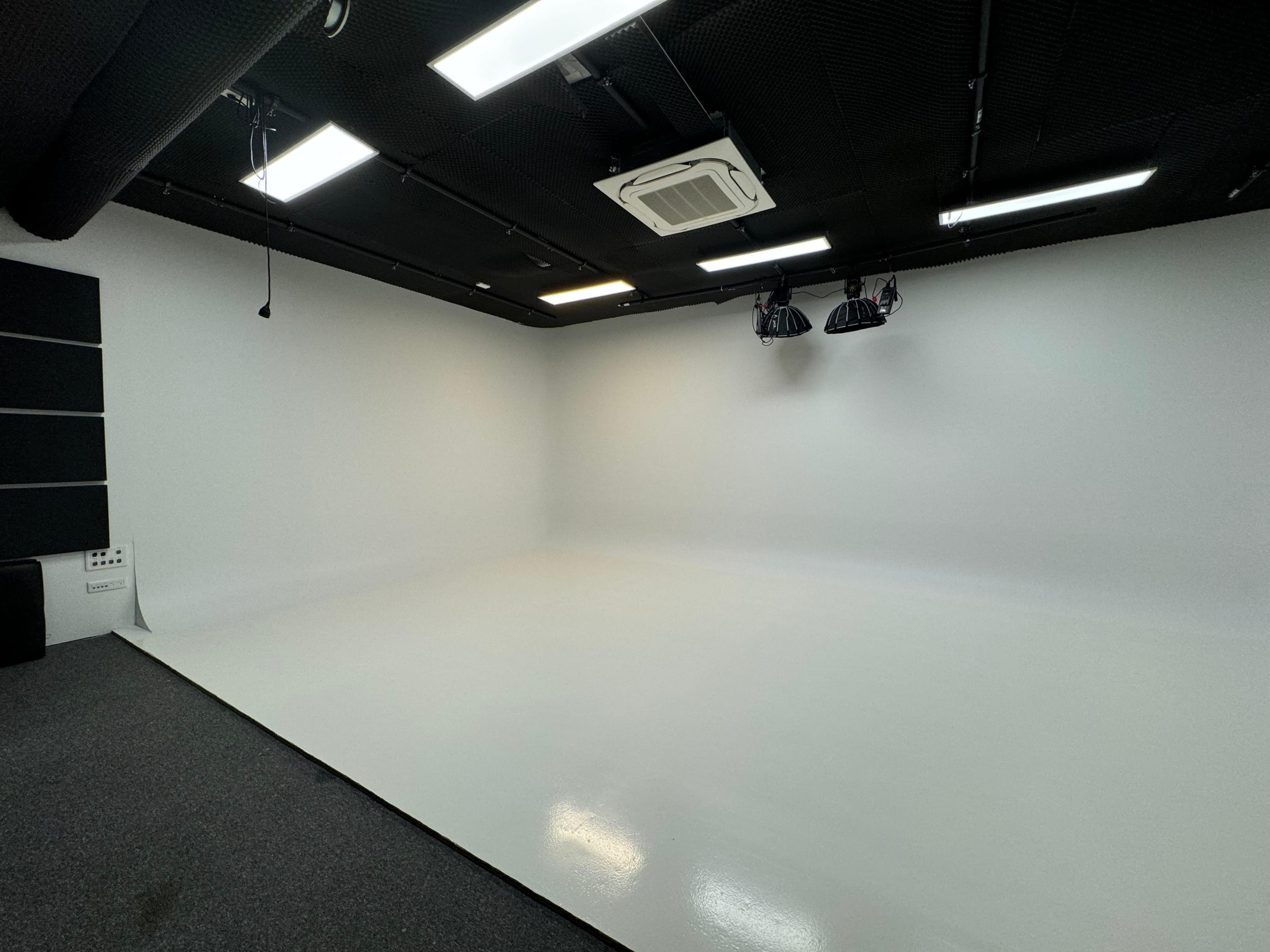 The image shows a blank, brightly lit studio space with a white floor and black ceiling.