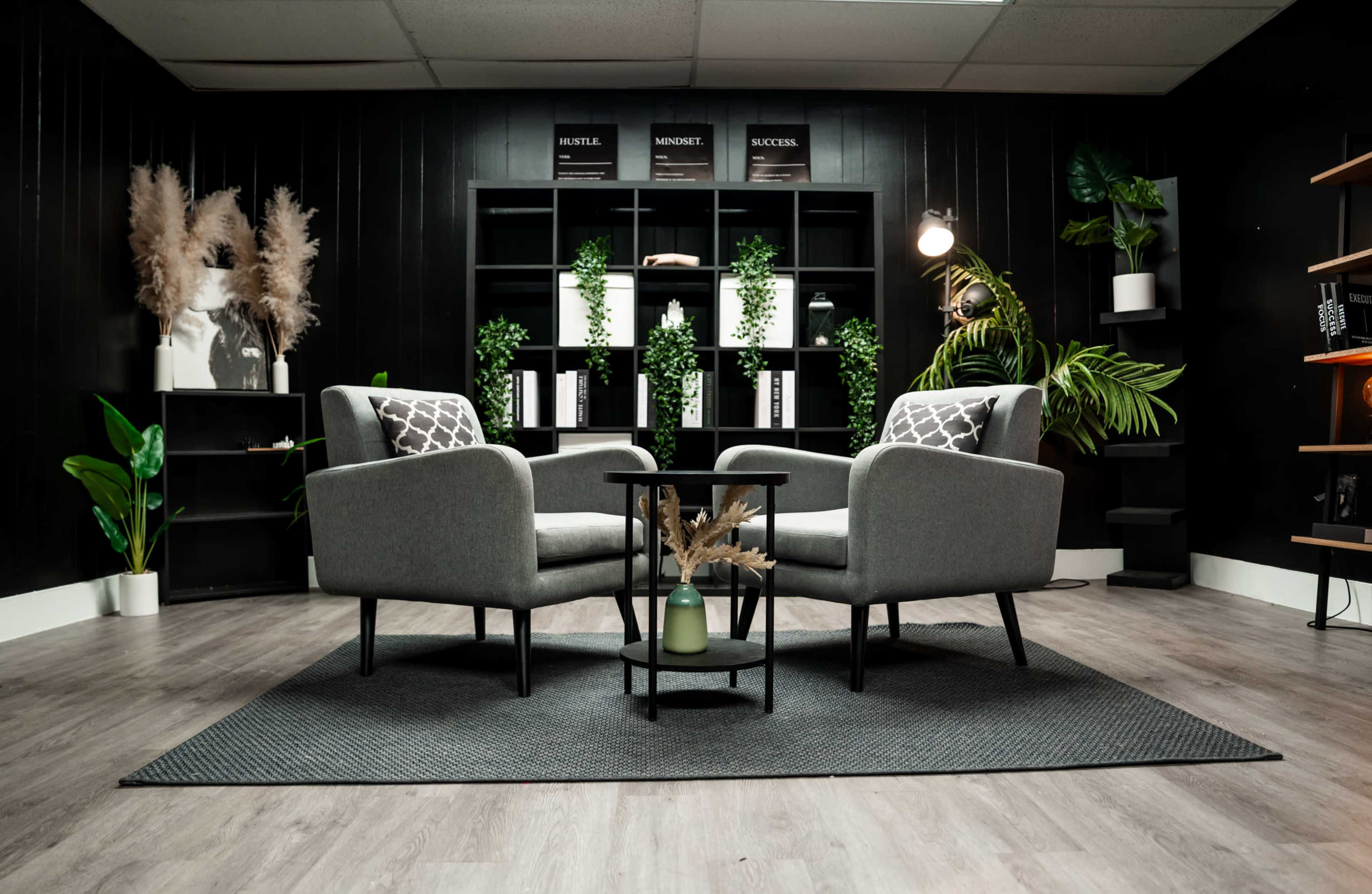 A modern seating area features two gray armchairs with patterned cushions arranged around a small black table on a textured rug.