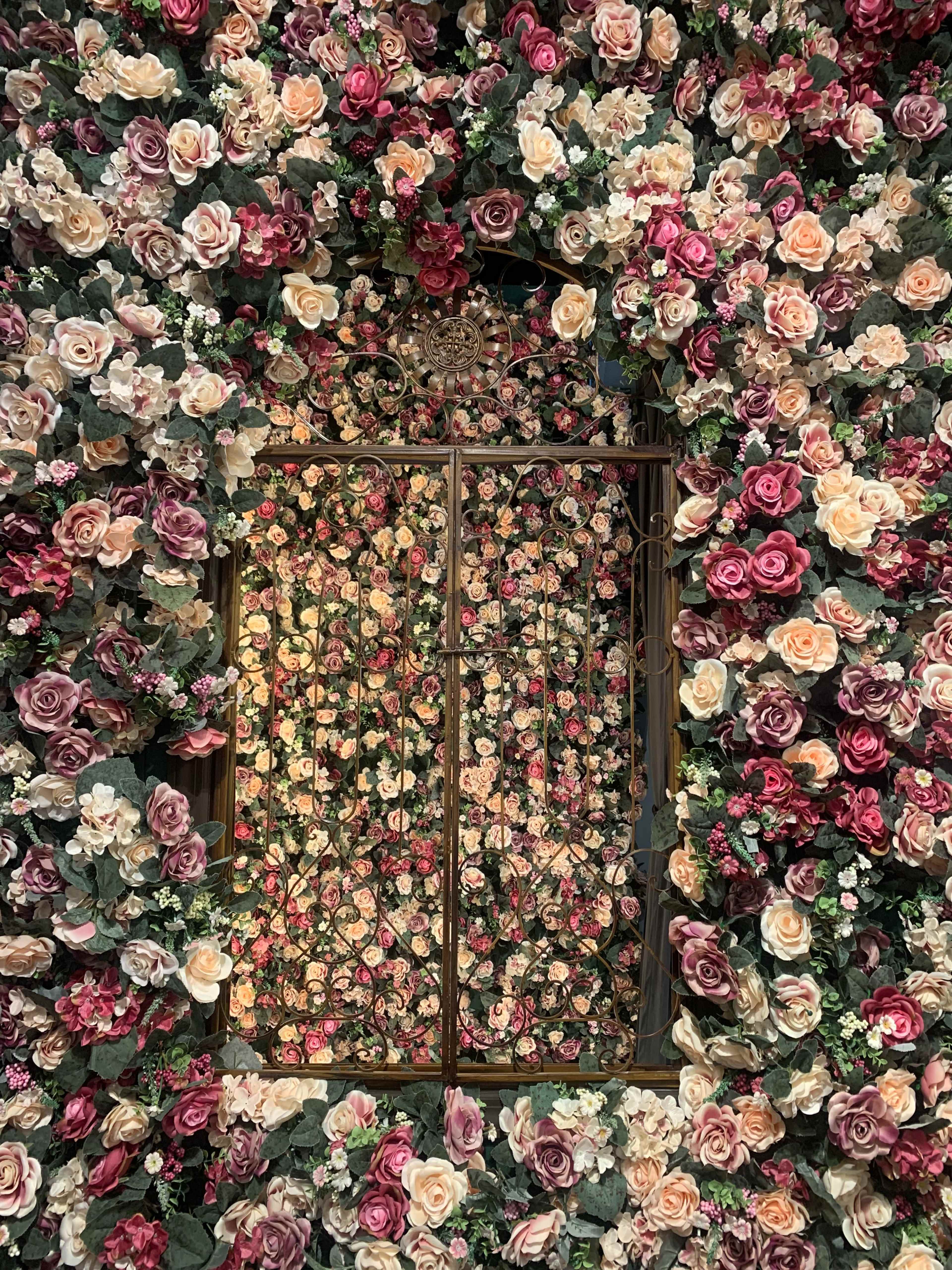 A wrought iron gate is partly covered by a dense arrangement of artificial roses and greenery.