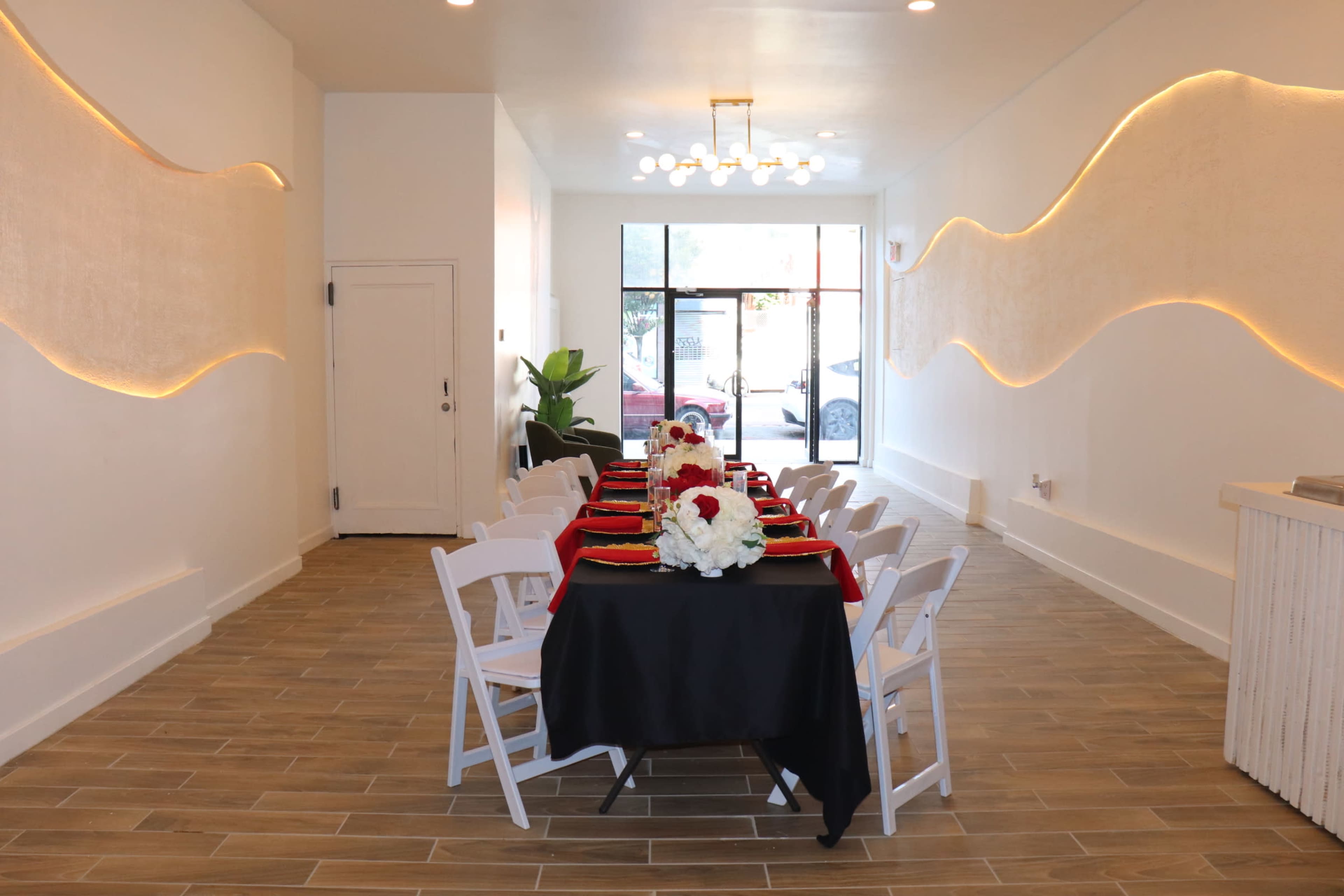 The image shows an elegantly set dining table with white chairs in a bright, modern interior space featuring decorative wall lighting.