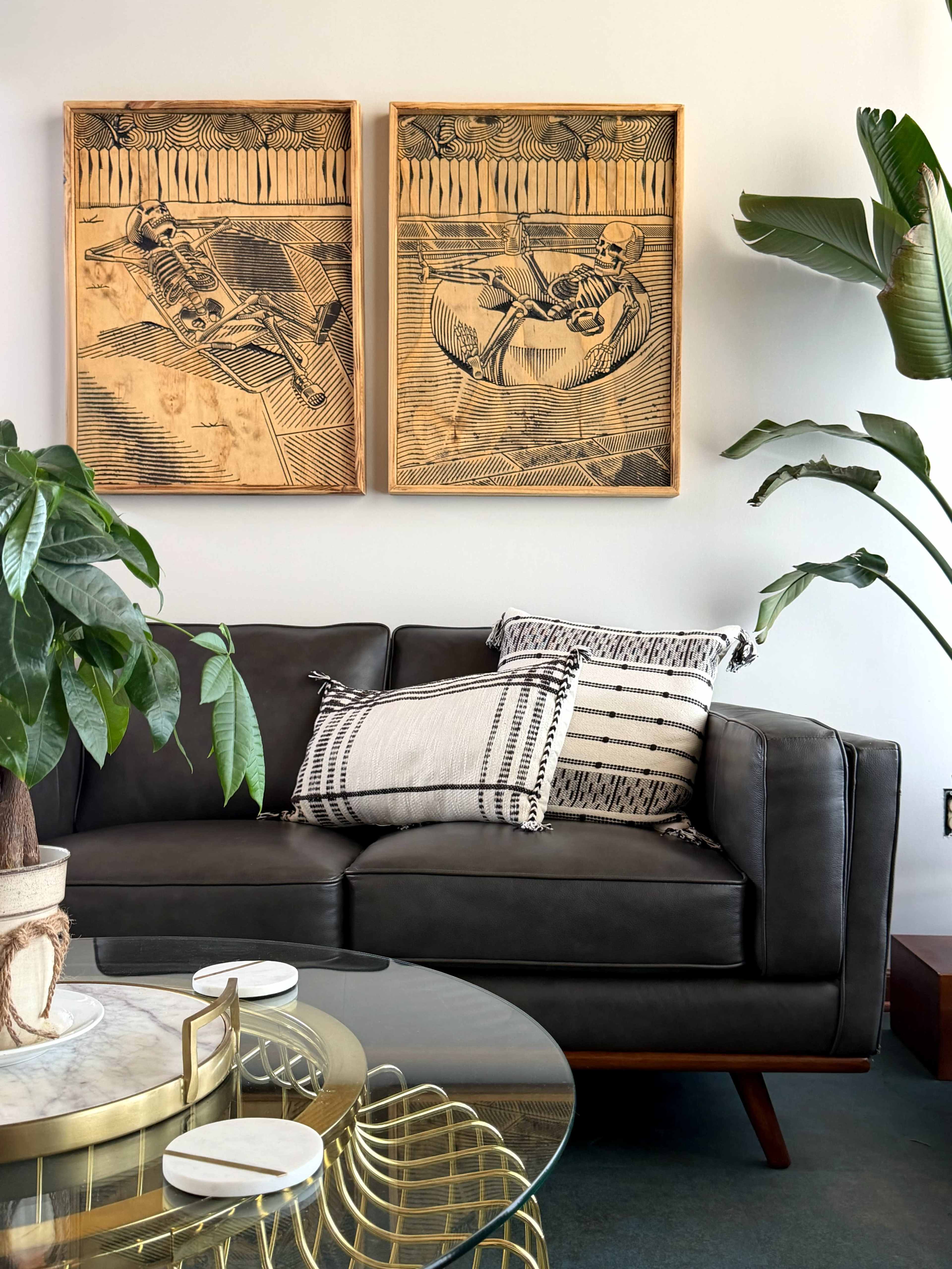 A modern living room features a dark leather sofa adorned with a patterned pillow, alongside two framed artworks on the wall and a round glass coffee table.