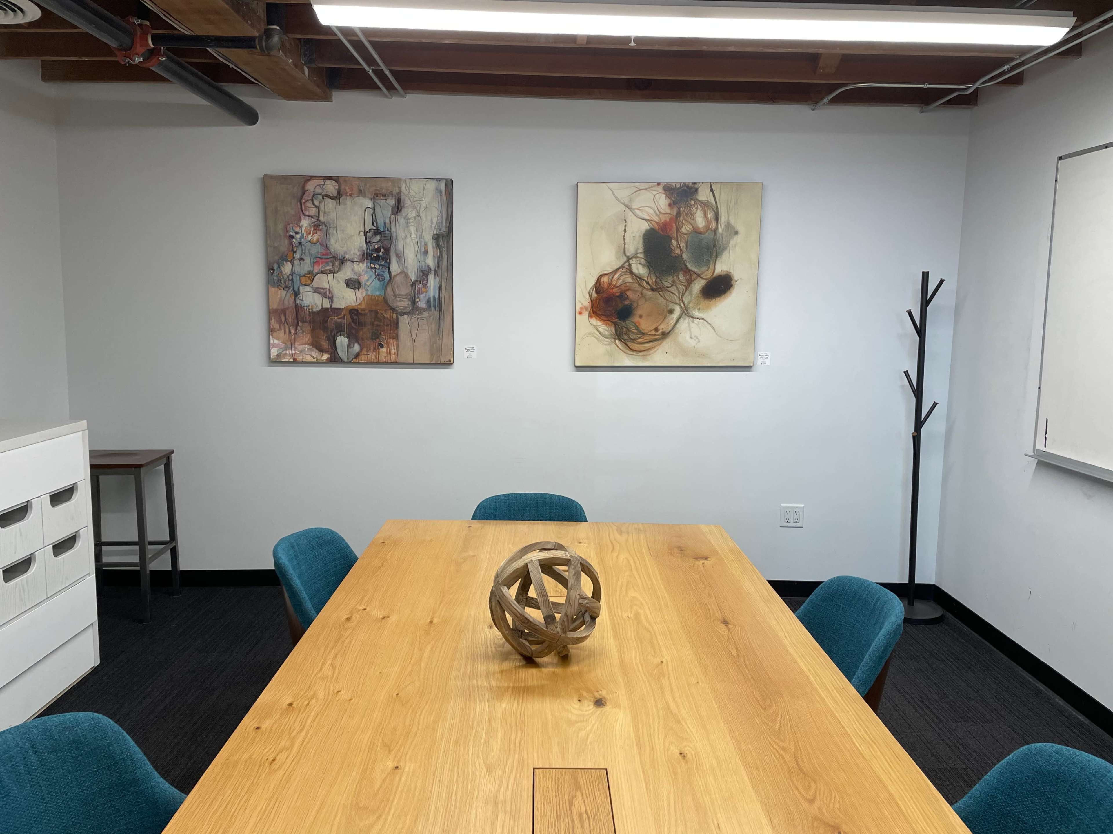 A conference room features a wooden table surrounded by blue chairs, with abstract wall art and a decorative sculpture in the center.