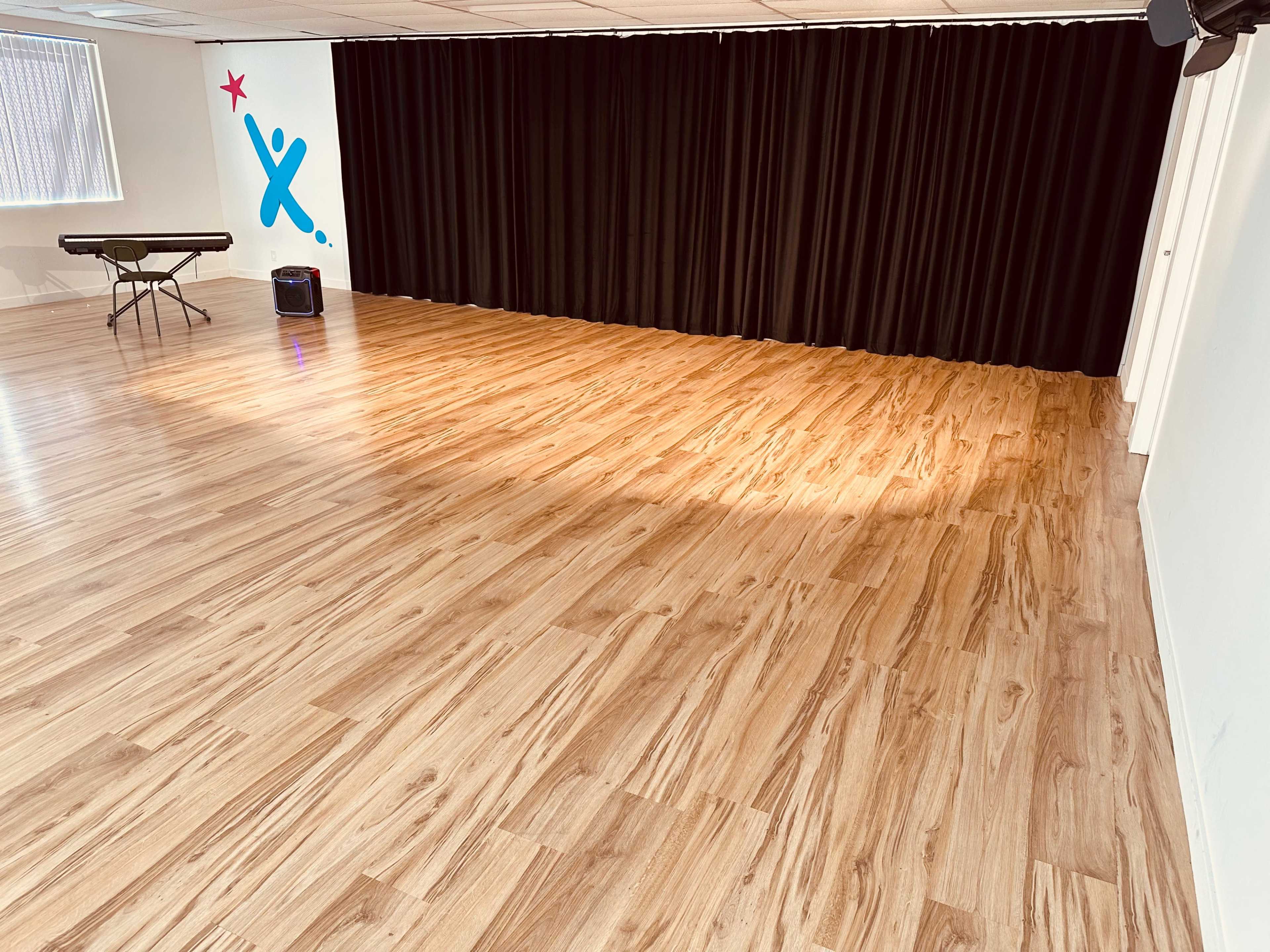 A spacious room with a hardwood floor, a small folding table on the left, and a black curtain along the back wall.