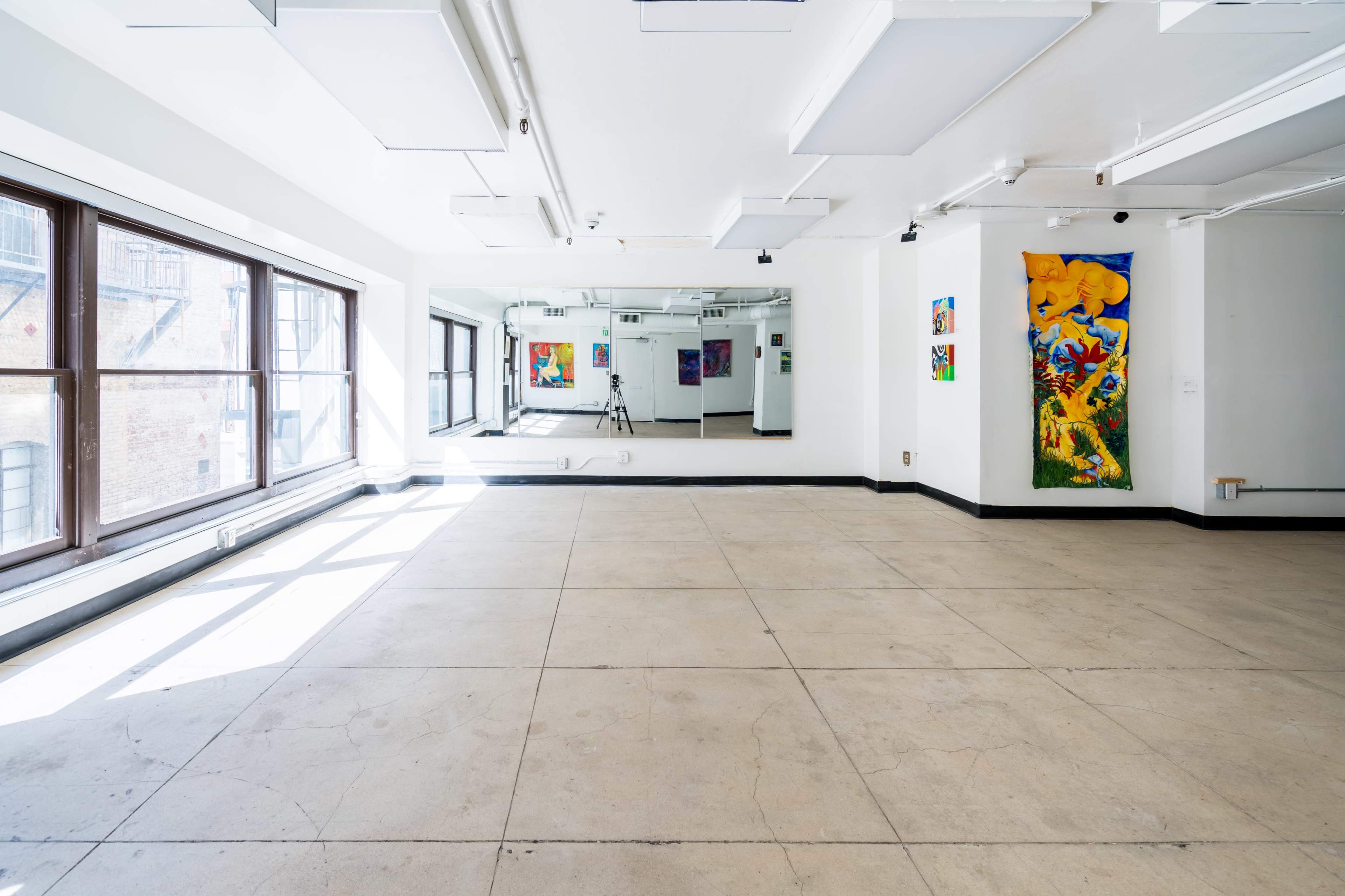 A spacious, empty studio with large windows and colorful artwork on the walls.